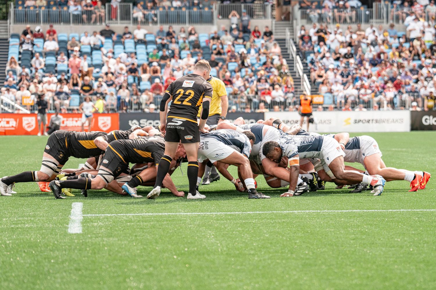 Rugby players engage in a scrum during a competitive match in a packed stadium on a sunny day.