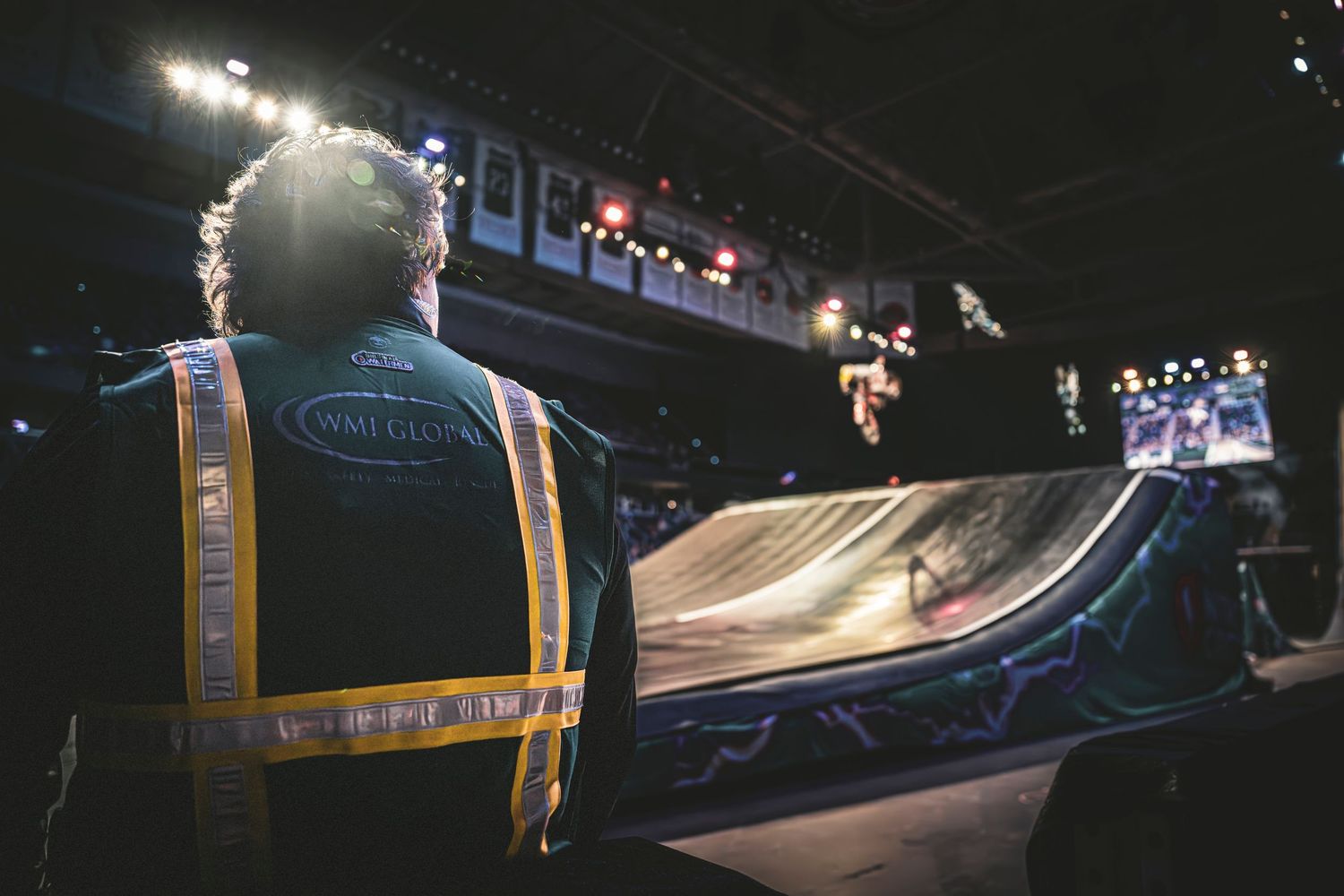 Safety worker in reflective vest monitors an indoor ski ramp at a nighttime event.