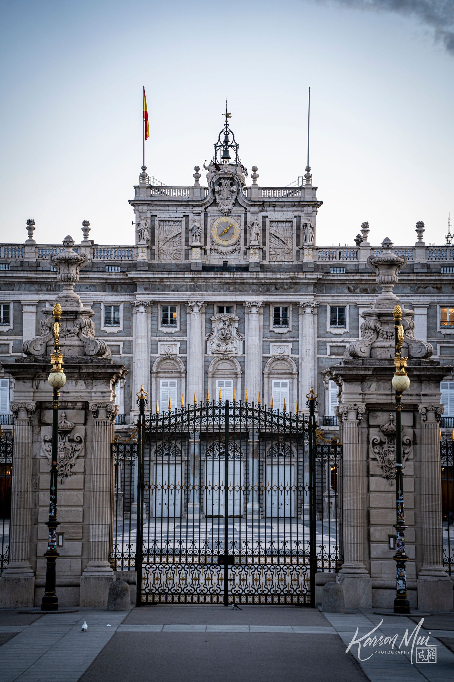 Ornate iron gates of the Royal Palace of Madrid at dusk with Spanish flag.
