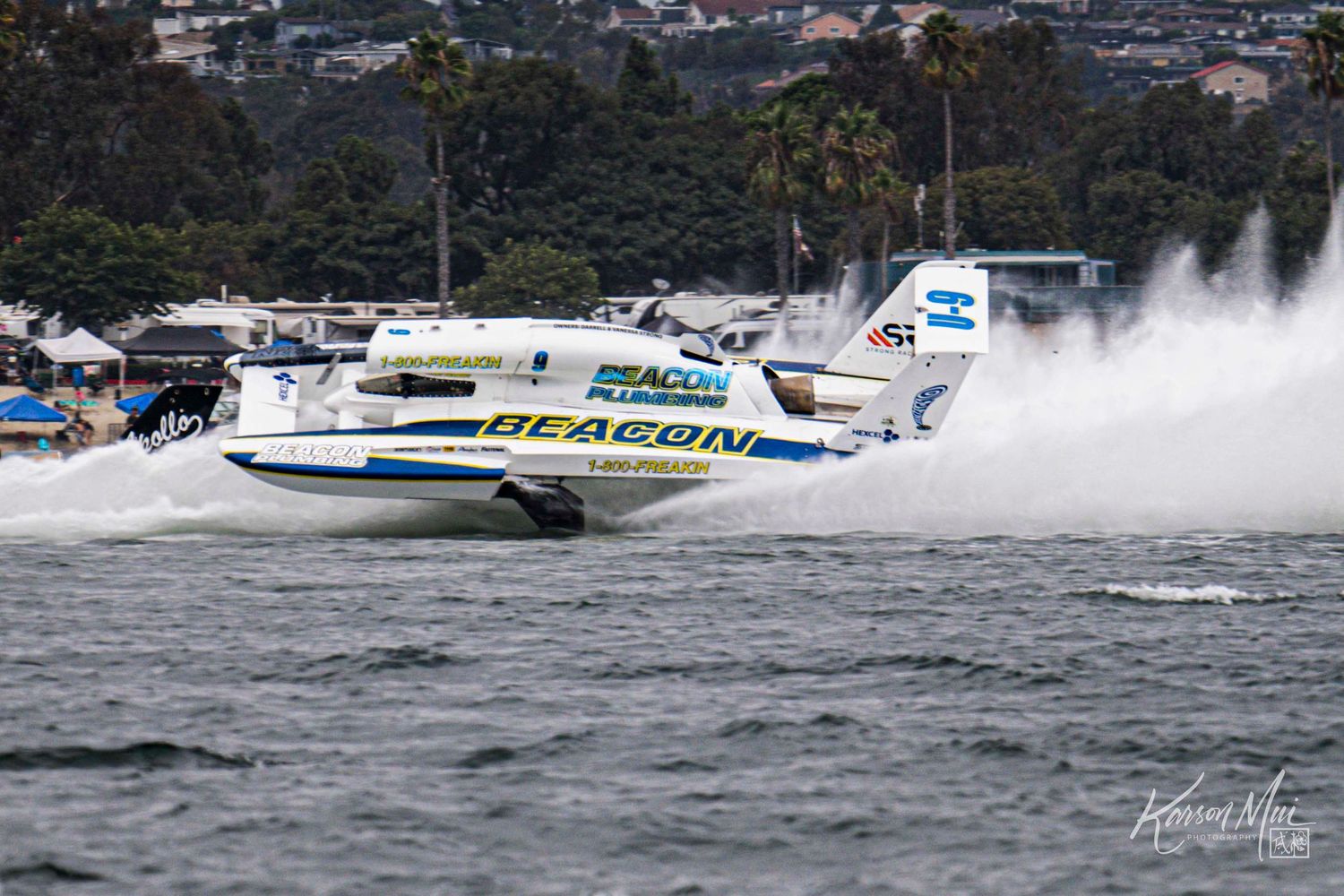 Two Beacon-sponsored racing powerboats compete side by side at high speed during a coastal race.