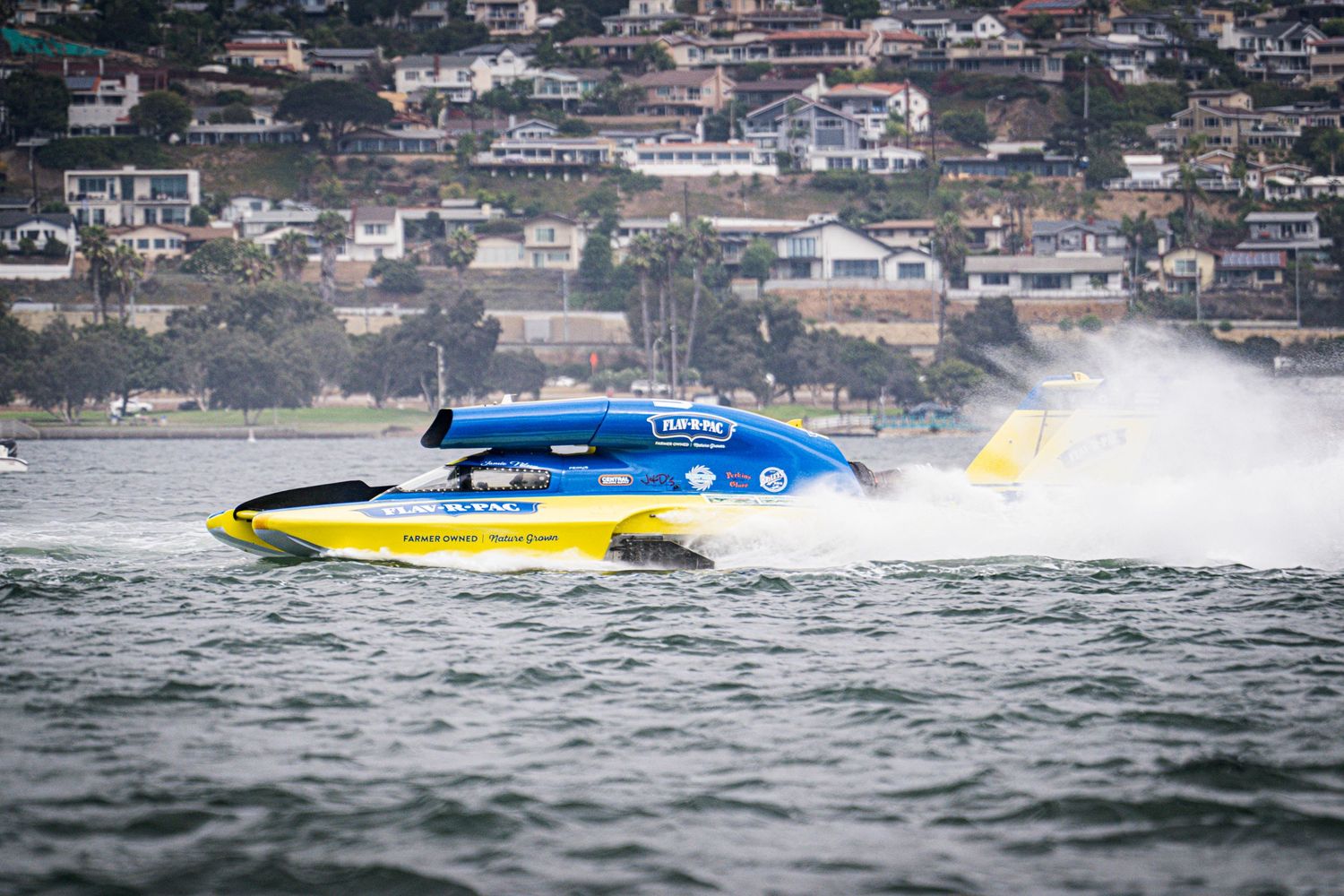 Yellow and blue racing powerboat speeds through choppy coastal waters during a powerboat race.