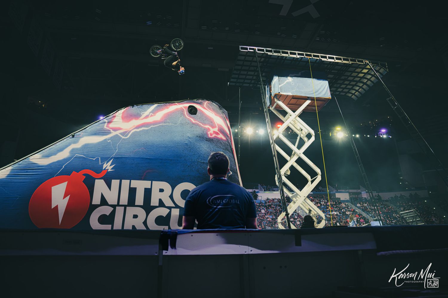 Person sits at a control booth overlooking a Nitro Circus arena event with a scissor lift and stage lighting.