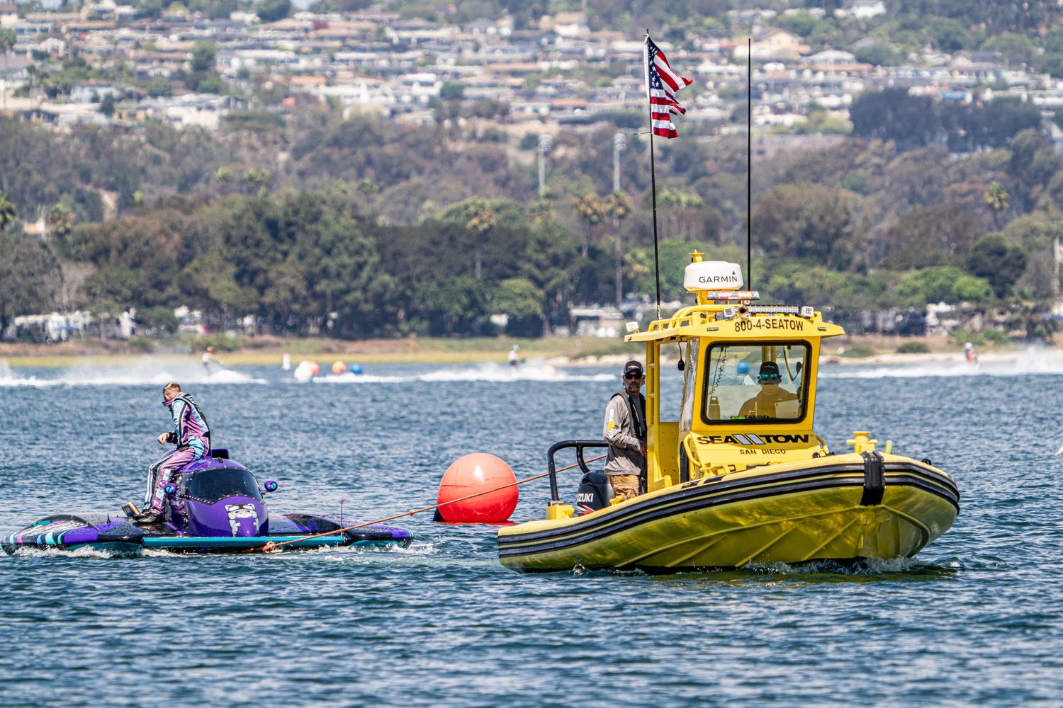 Purple racing boat near orange buoy with yellow safety vessel on open water.