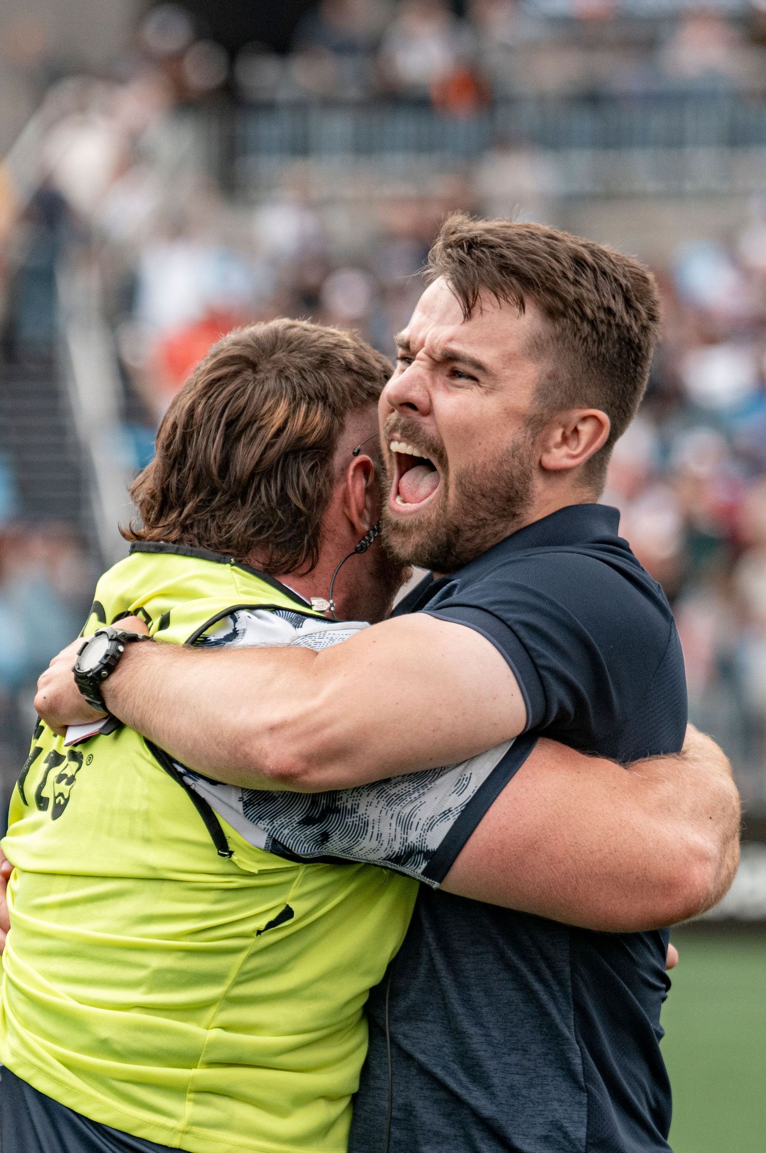 Two men share emotional celebratory hug after winning sports match in stadium setting.