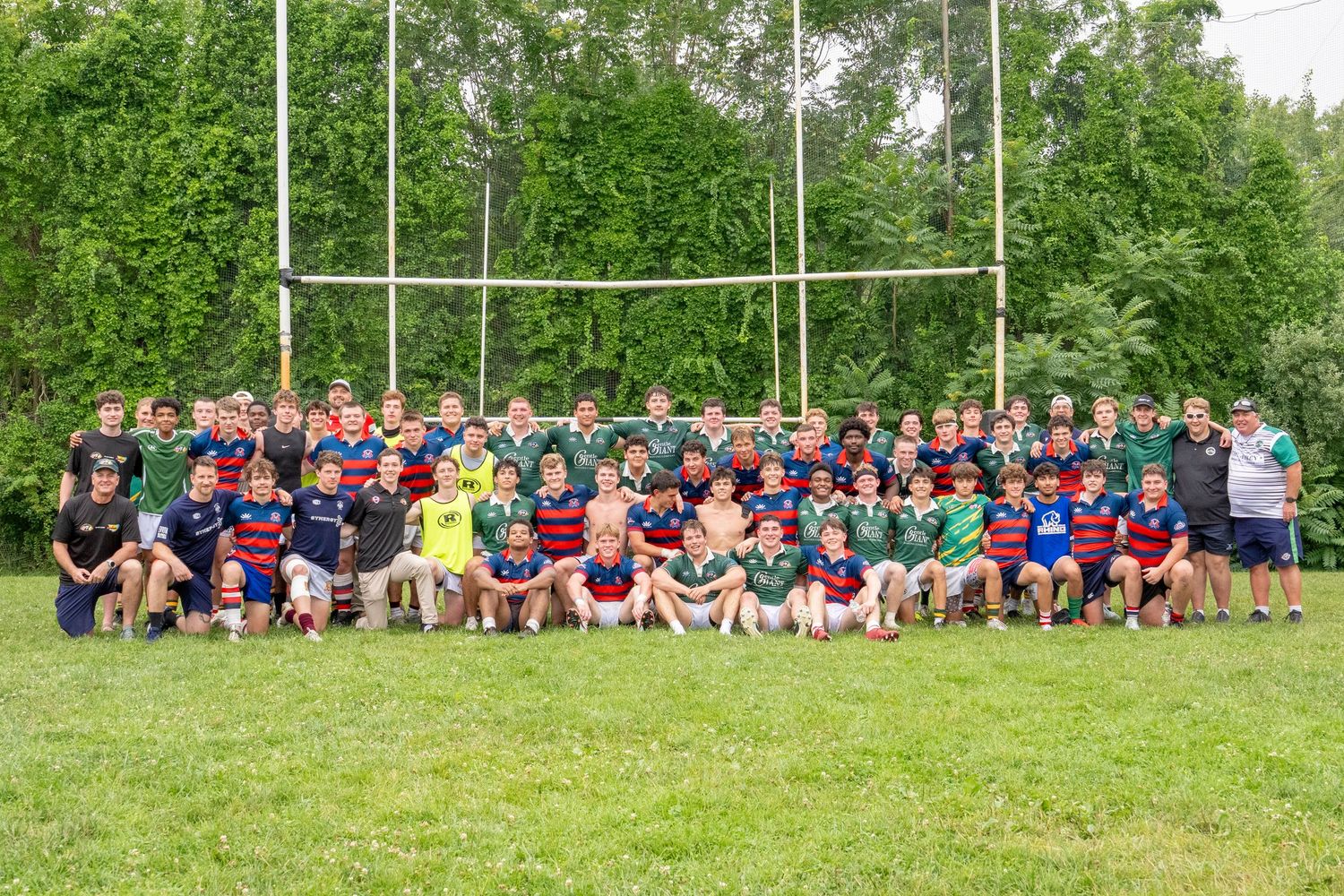 Large youth rugby team poses together on a grass field in front of goalposts after a match.