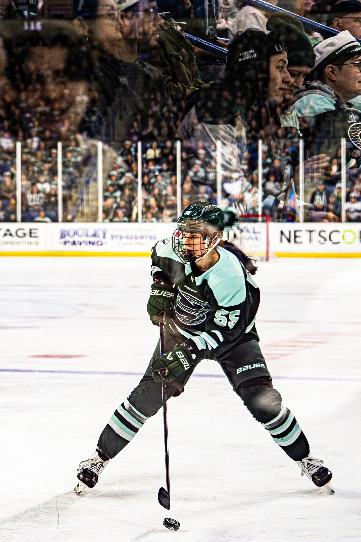 Female hockey player in teal uniform takes a shot on ice during a professional league game.