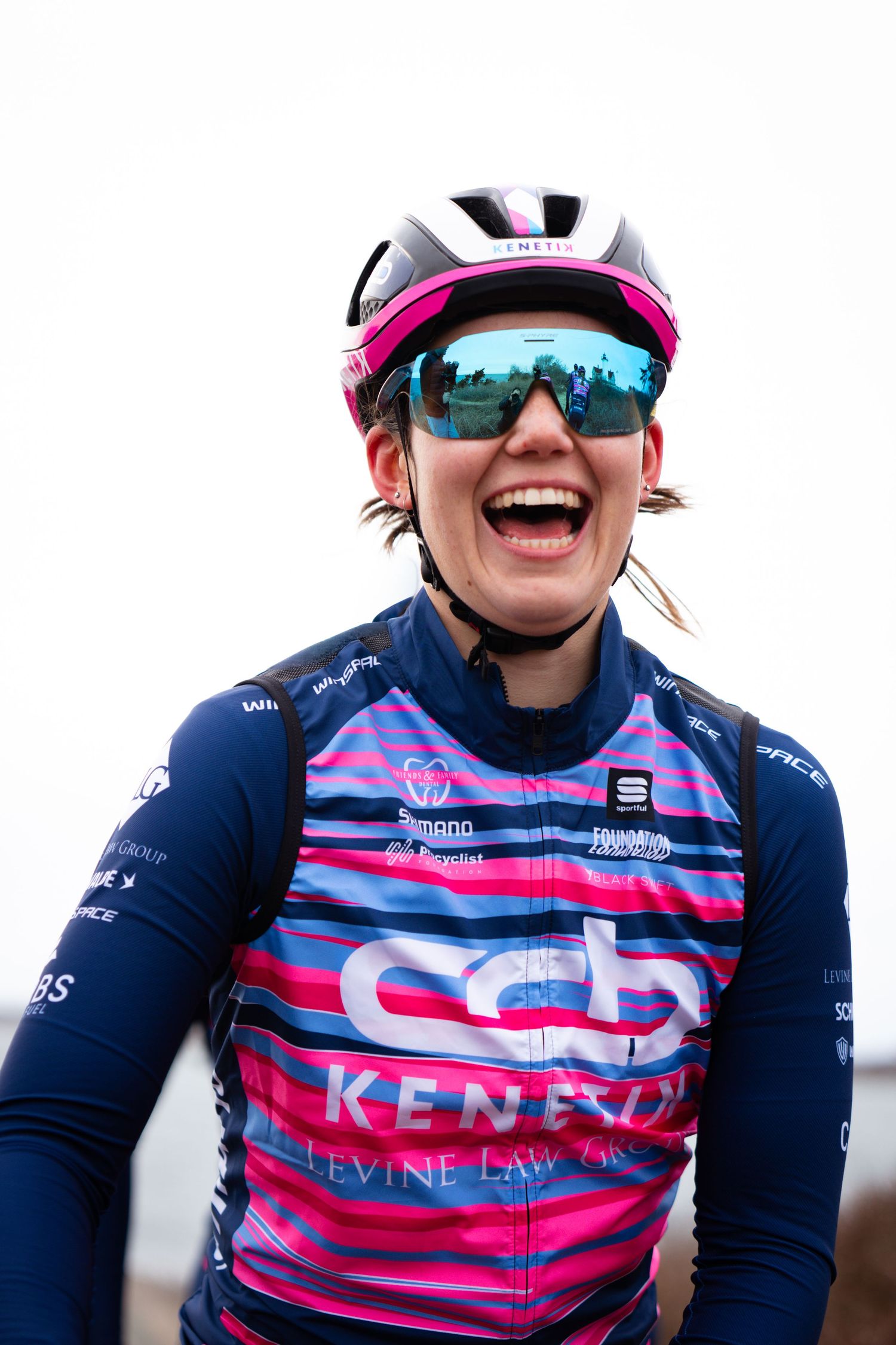Smiling female cyclist in CCB Kenetix team jersey and helmet with blue mirrored sunglasses.