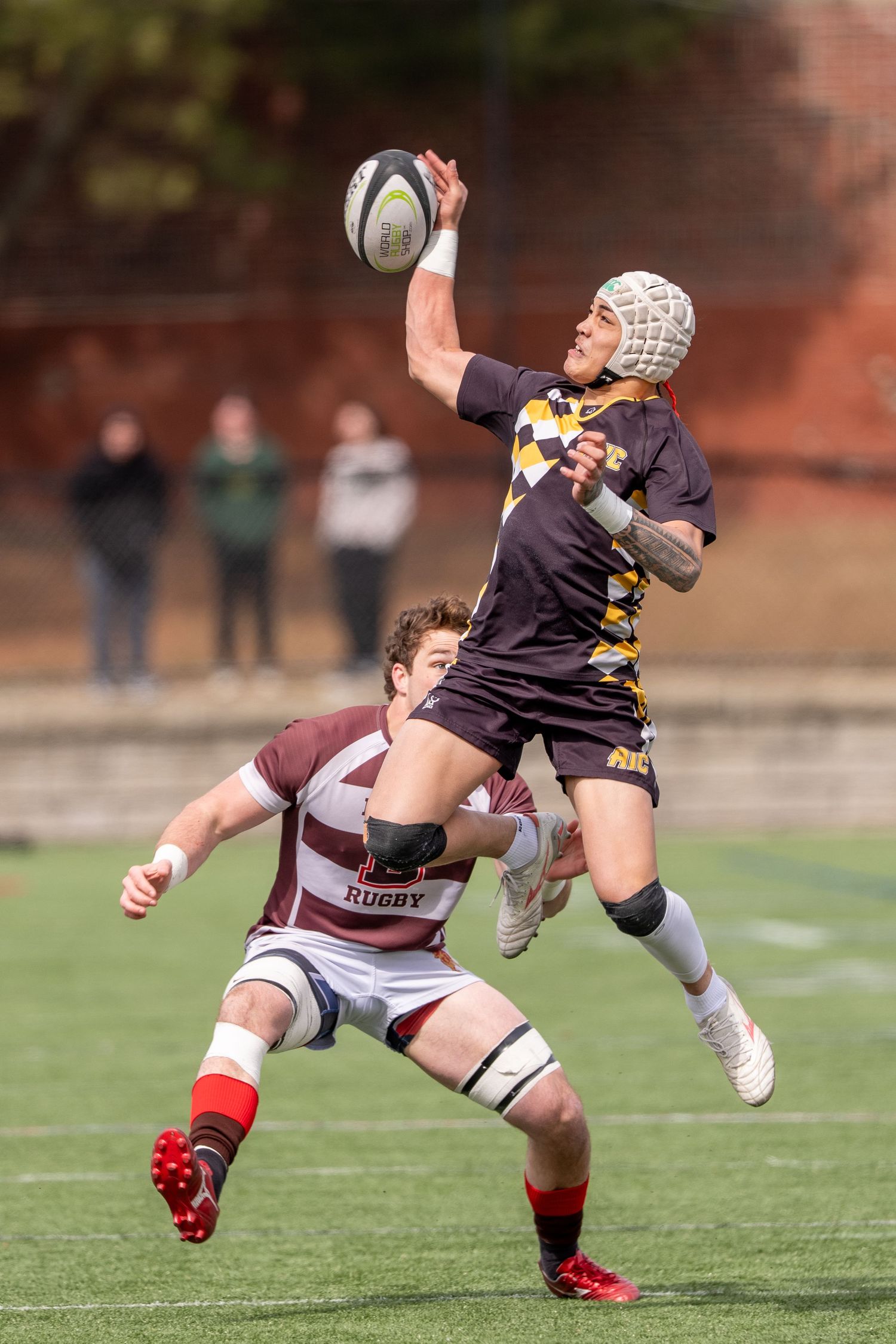 Rugby player leaps to catch the ball during an intense collegiate match on a sunny day.