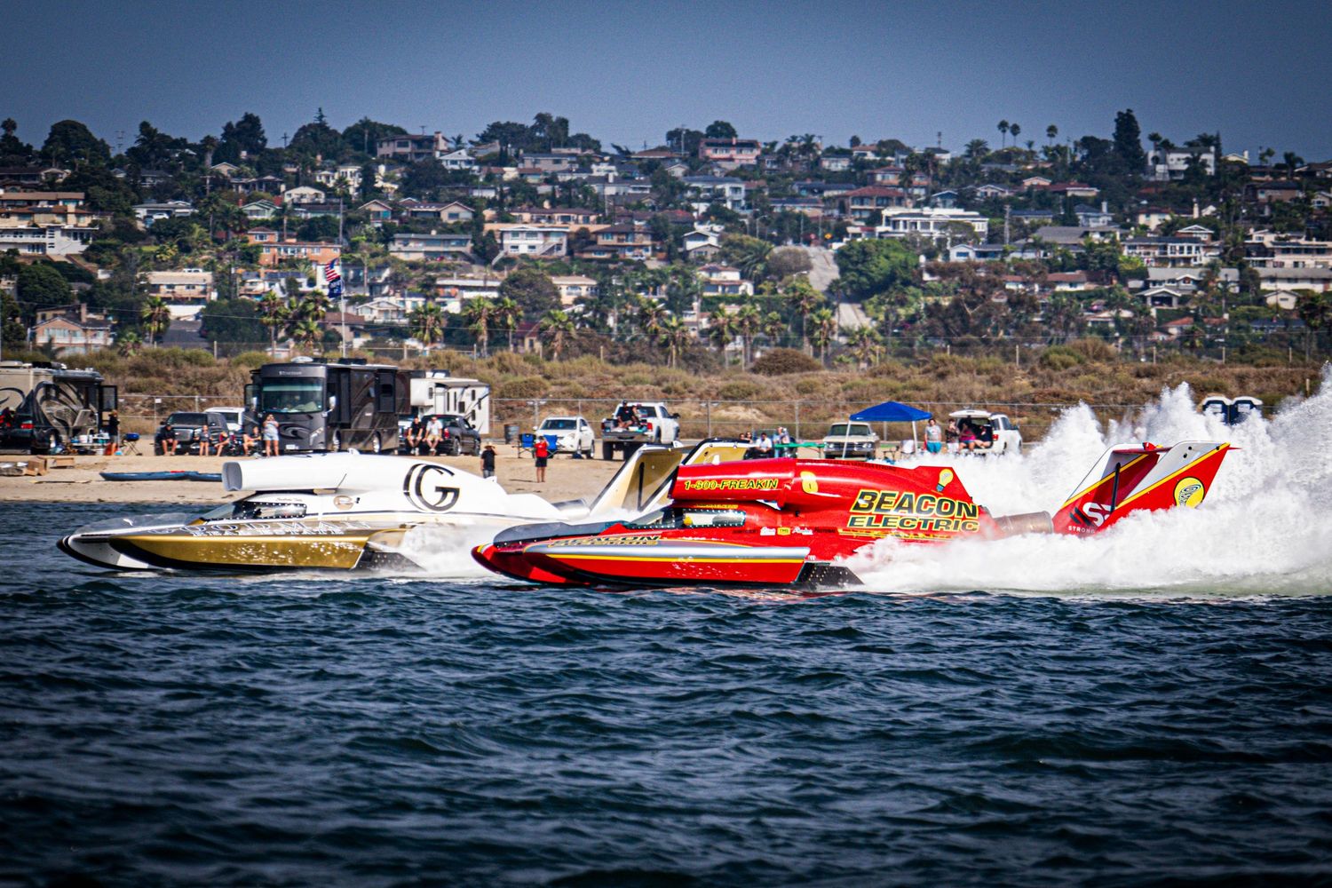 Red and white powerboats race across choppy water at a high-speed boat racing event near a coastal town.