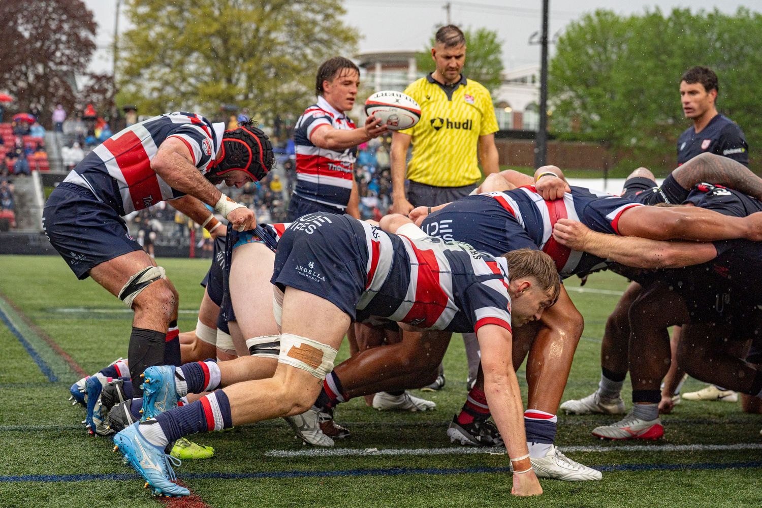 Rugby players contest a scrum as a referee watches closely during a competitive outdoor match.