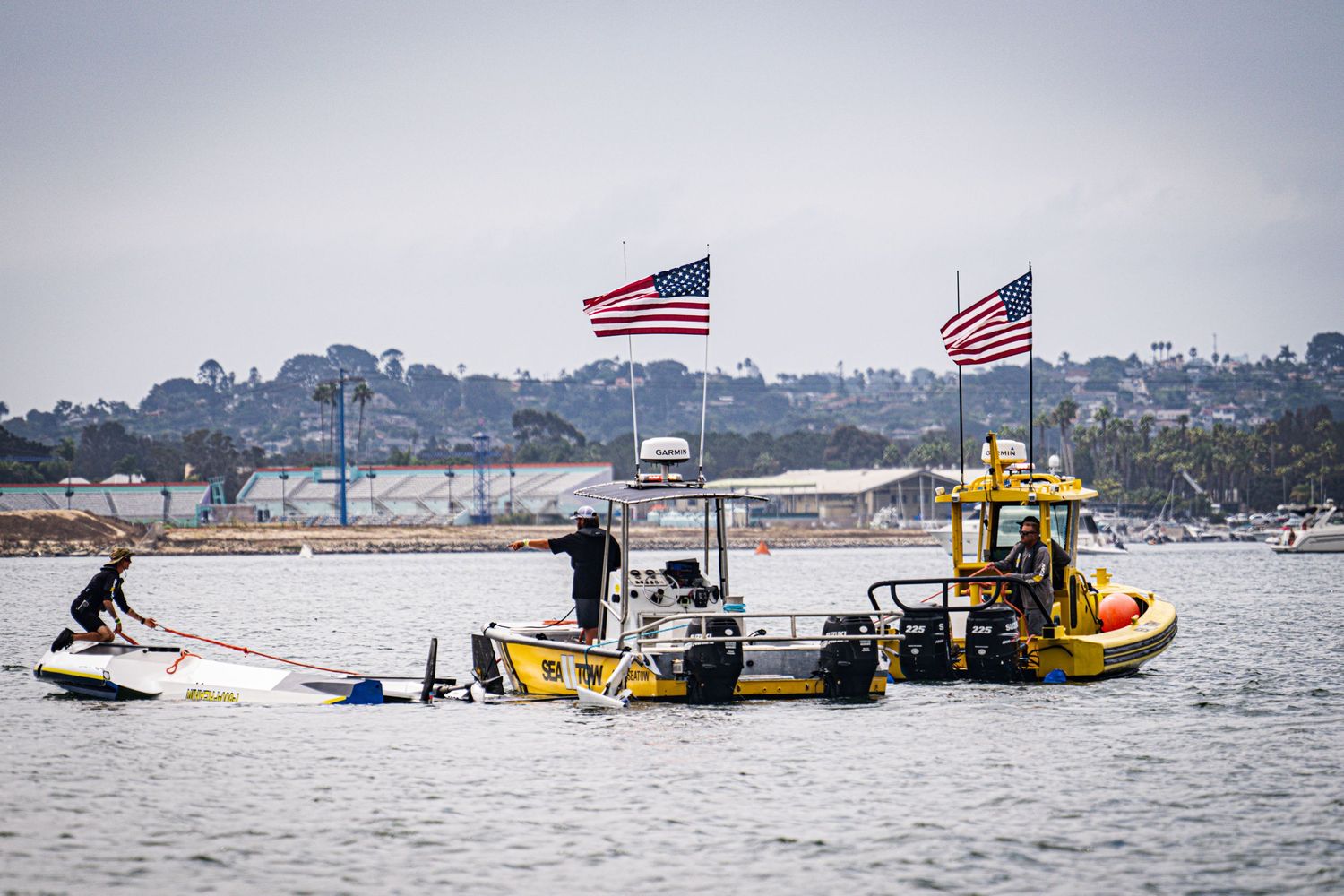 Coast Guard rescue boats with American flags respond to an overturned watercraft in a calm bay.