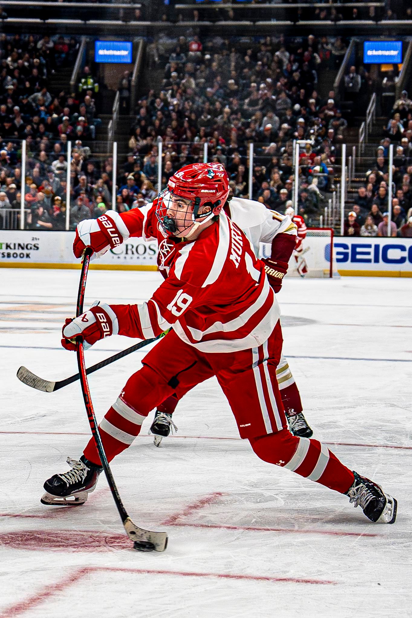 Boston University Terriers player number 19 takes powerful shot during college hockey game.