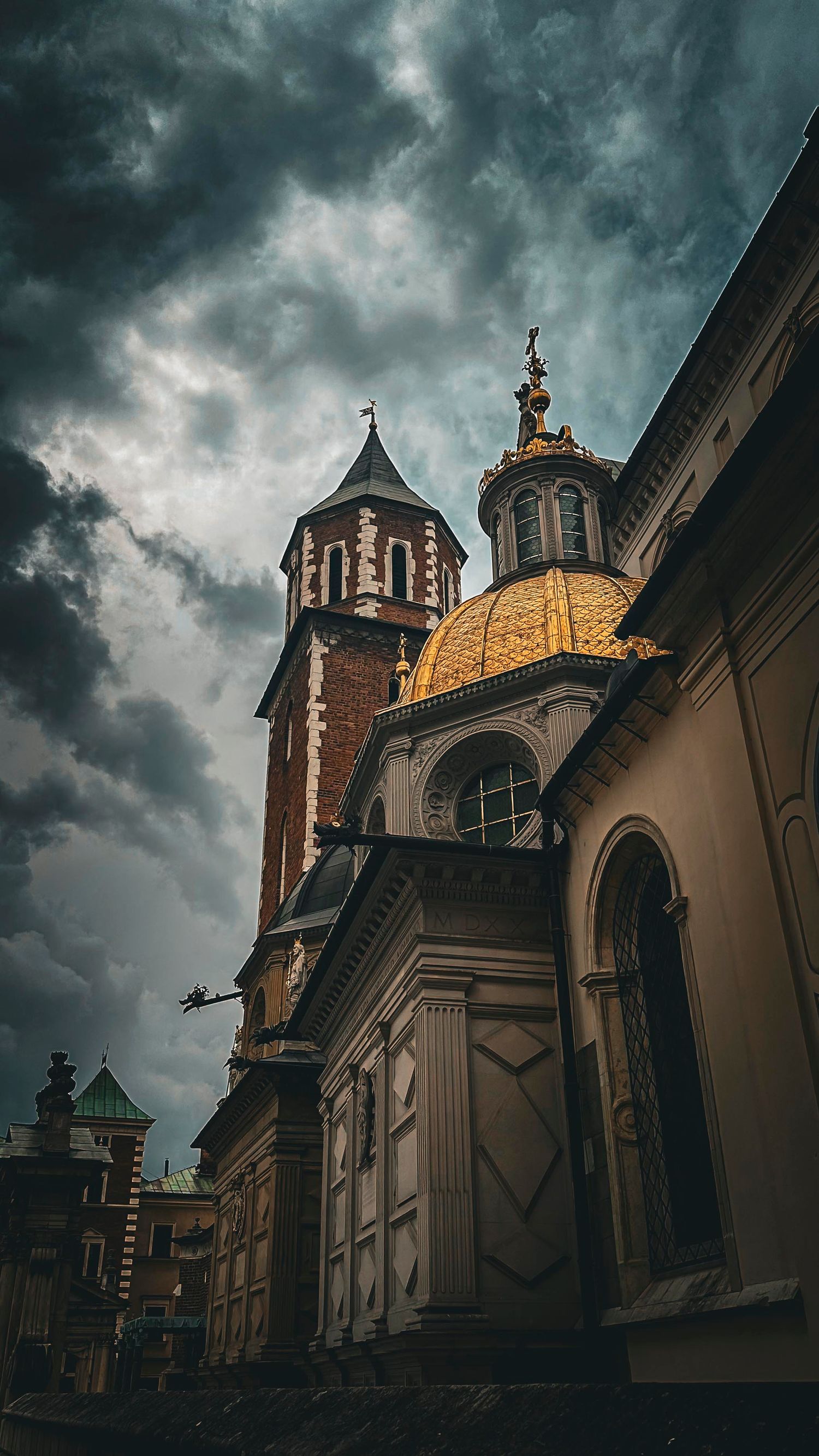 Gothic church with golden dome and brick tower under dramatic stormy sky in Krakow, Poland.