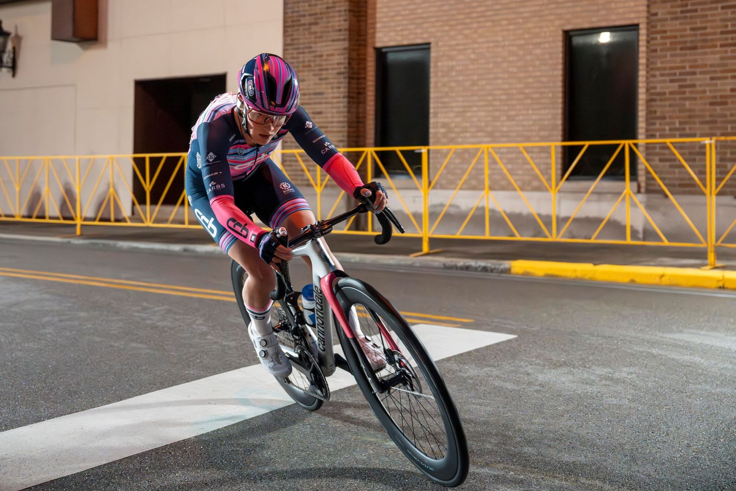 Cyclist in colorful racing kit rides a road bike through urban streets during a cycling race or training event.
