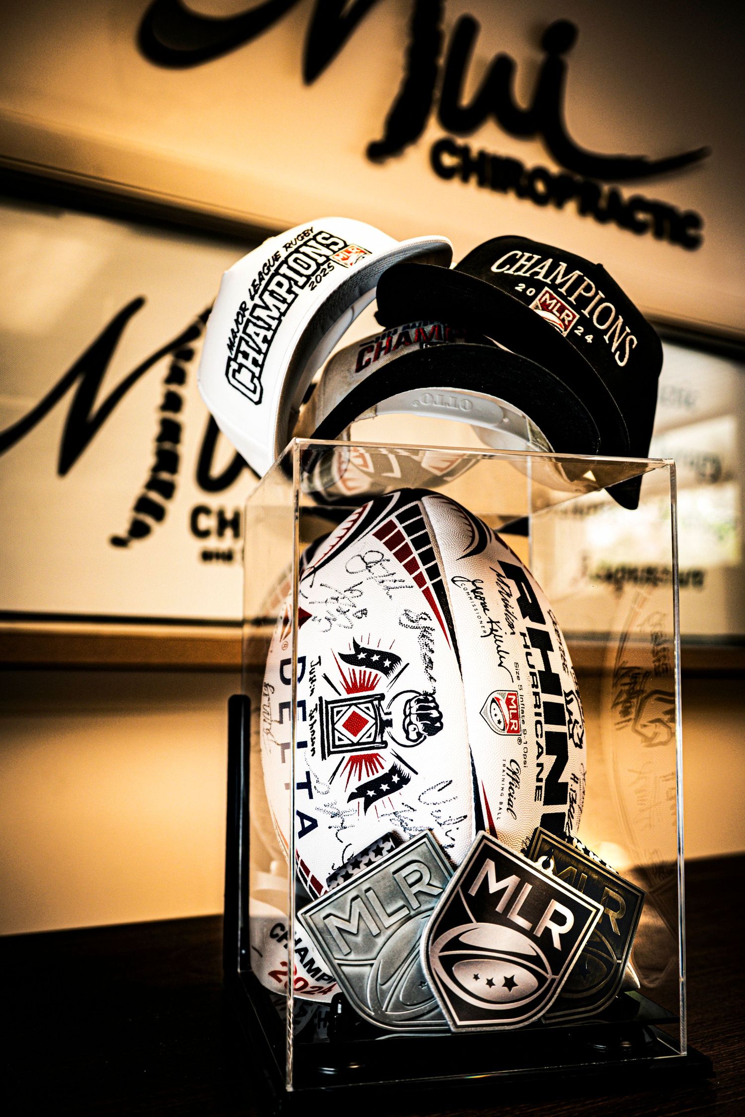 MLR Champions rugby ball and hats displayed in glass case at Mui Chiropractic office.