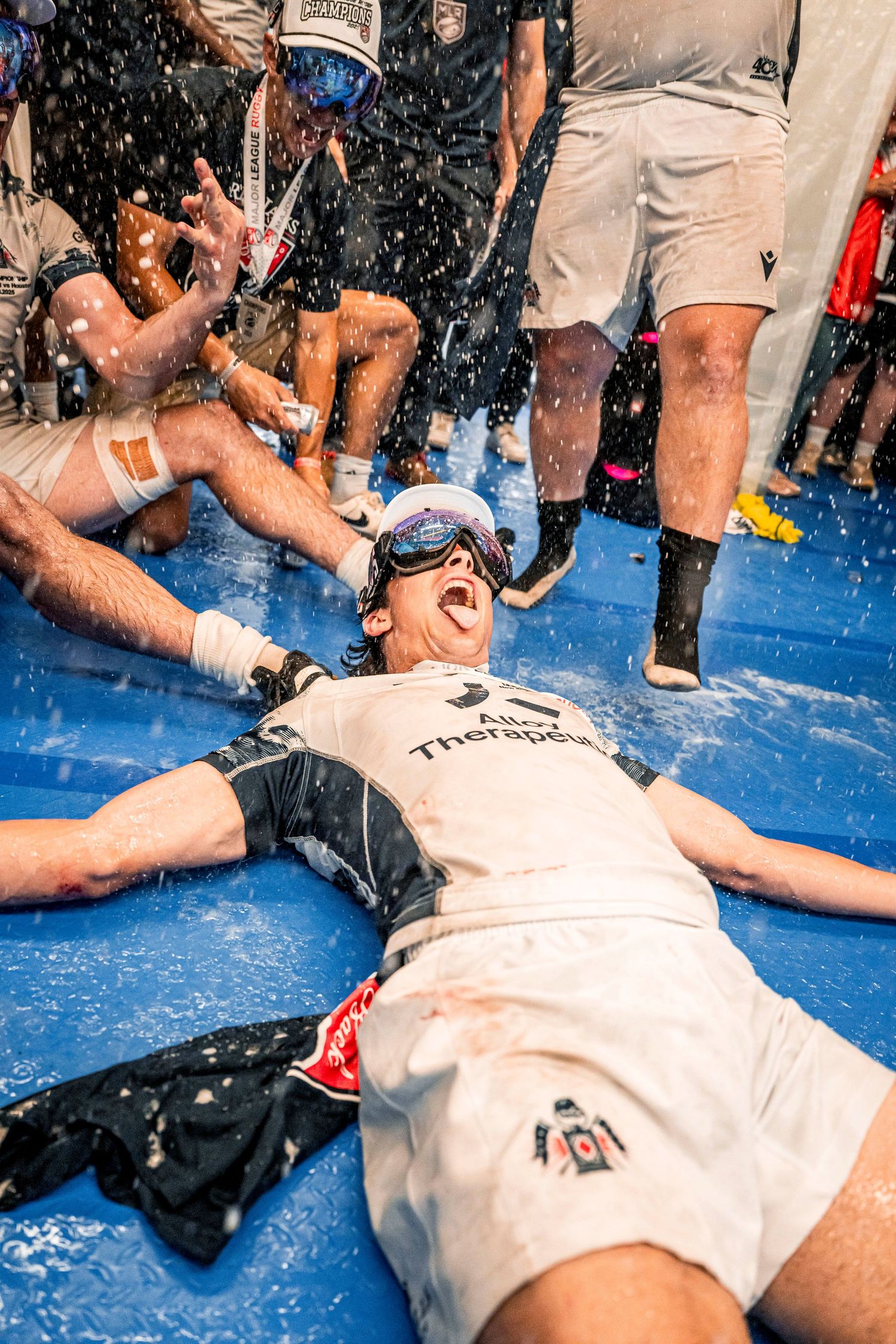 Athlete celebrates victory lying on floor covered in champagne spray during sports championship celebration.