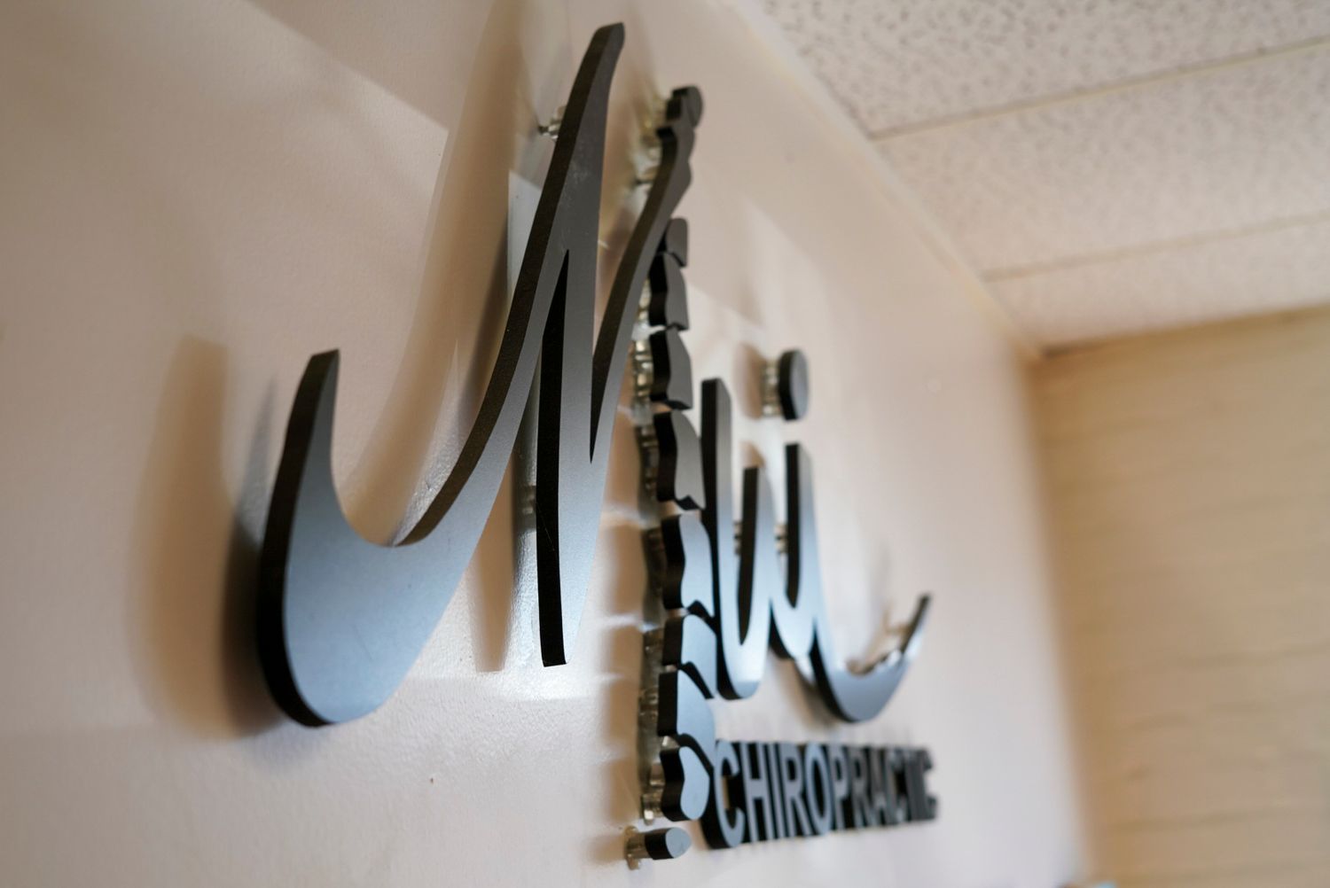 Metal script sign reading Merit Chiropractic mounted on a beige office wall with decorative spine illustration.