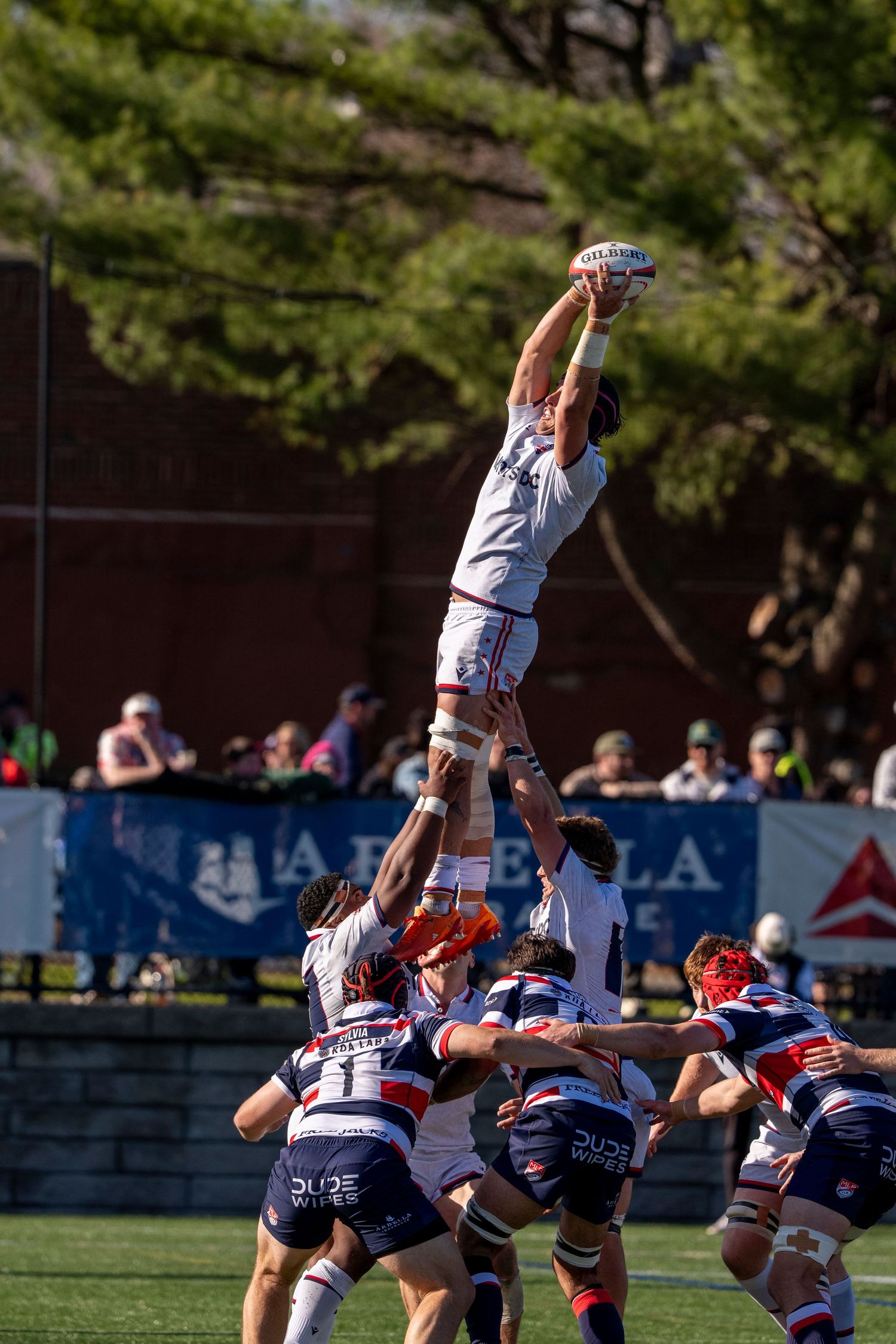 Rugby players compete in a lineout, with one player lifted high to catch the ball during an outdoor match.