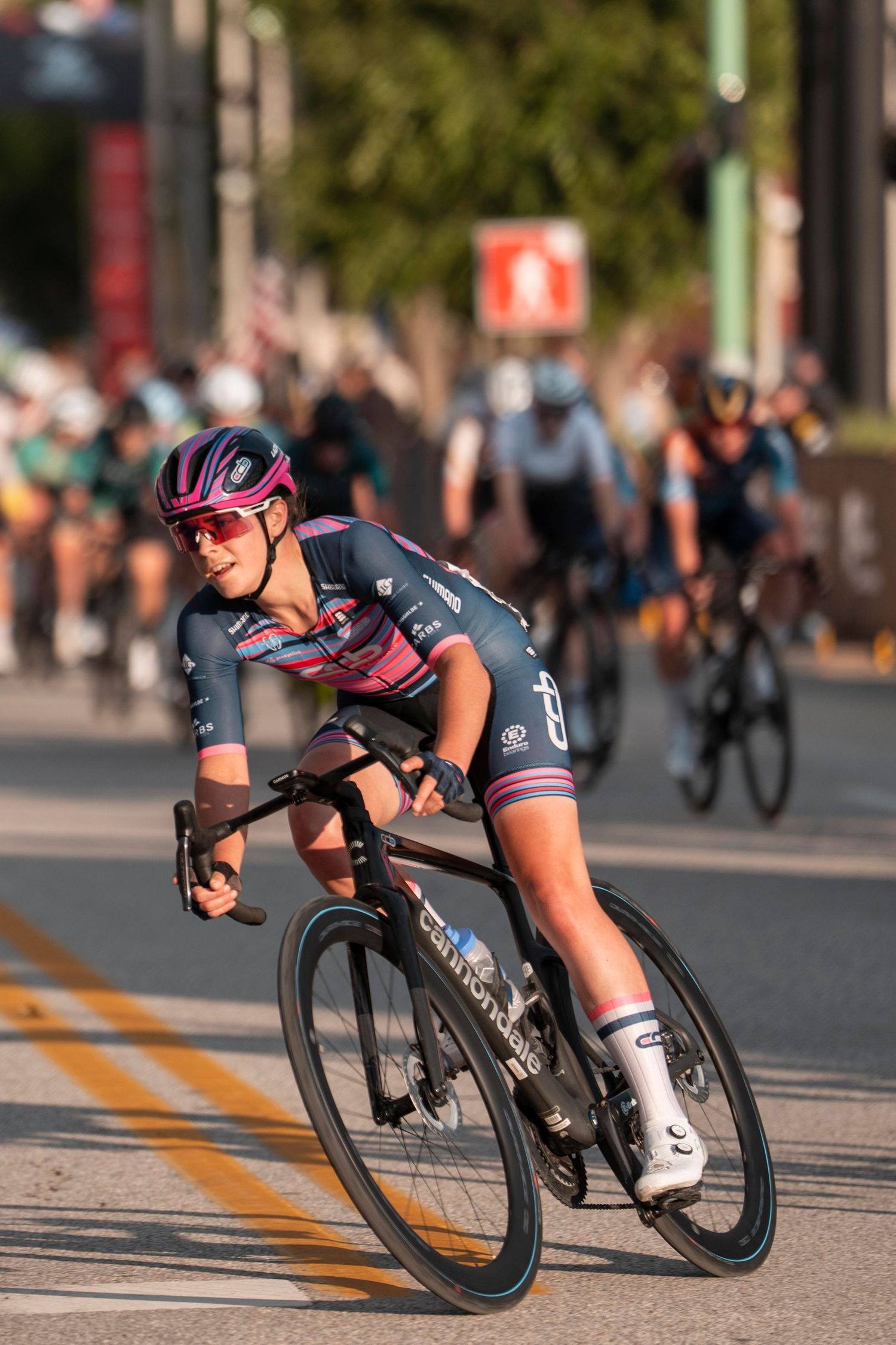 Female cyclist in pink and navy kit races ahead of competitors on a road cycling course.
