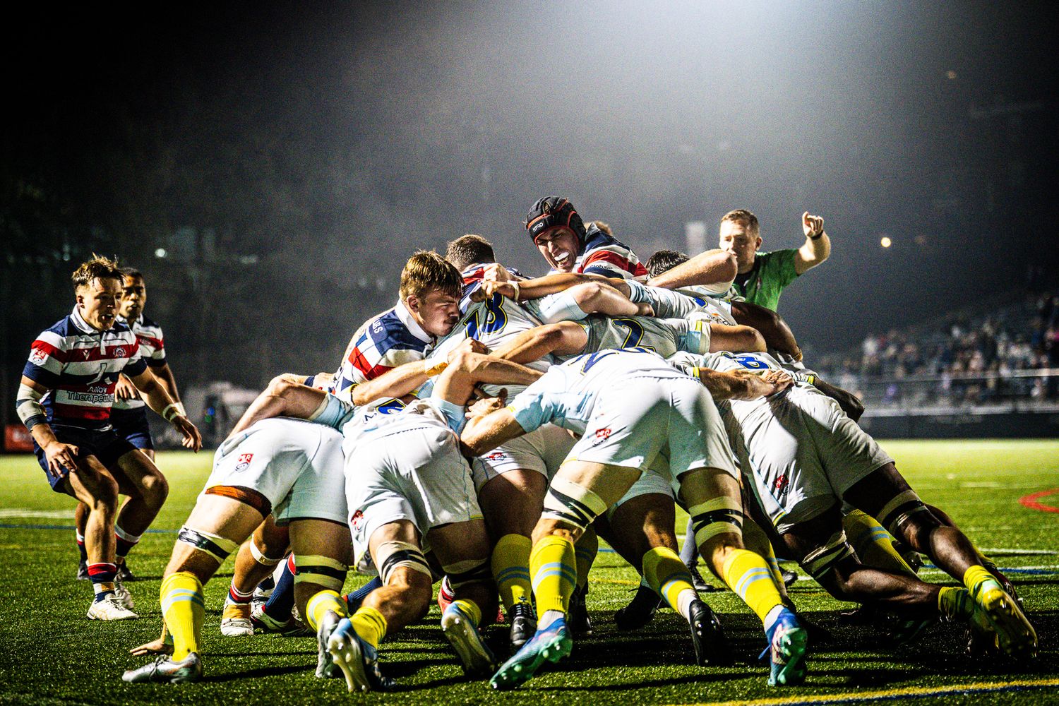 Rugby team forms a scrum under bright stadium lights during an intense night match.