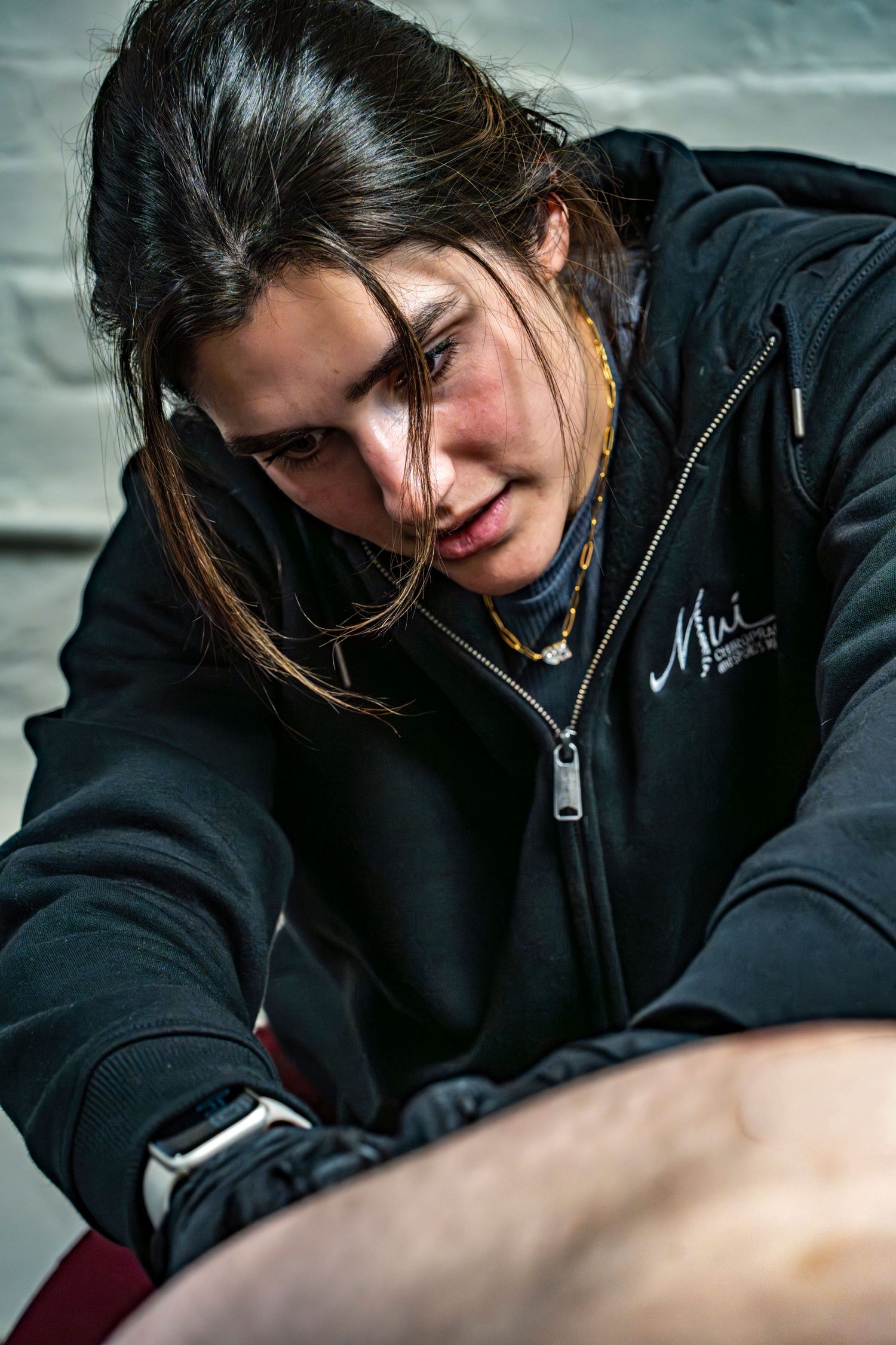 Young woman with dark hair in black hoodie focused on performing a tattoo procedure.