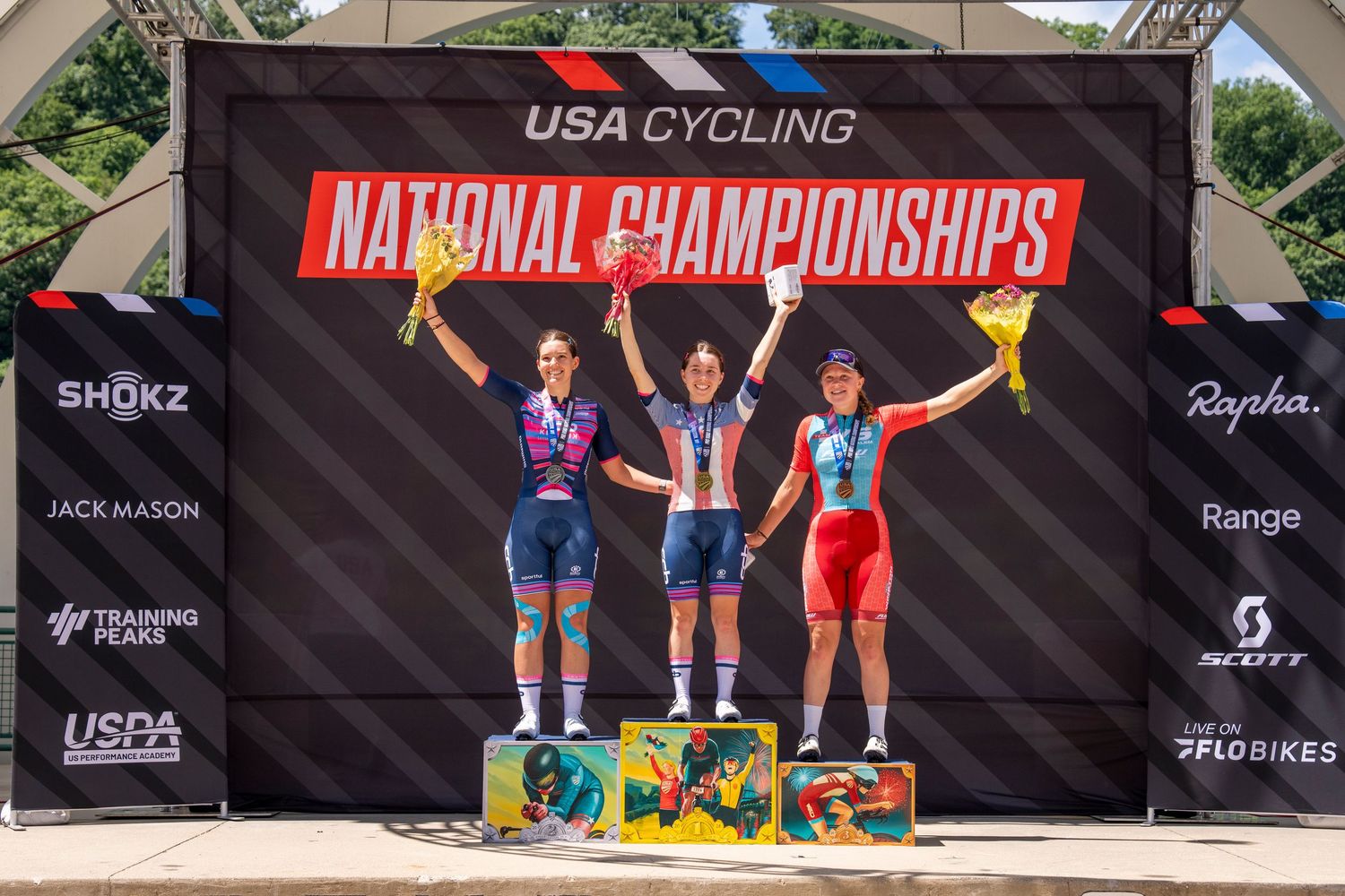 Three female cyclists celebrate on the USA Cycling National Championships podium, holding trophies and bouquets.