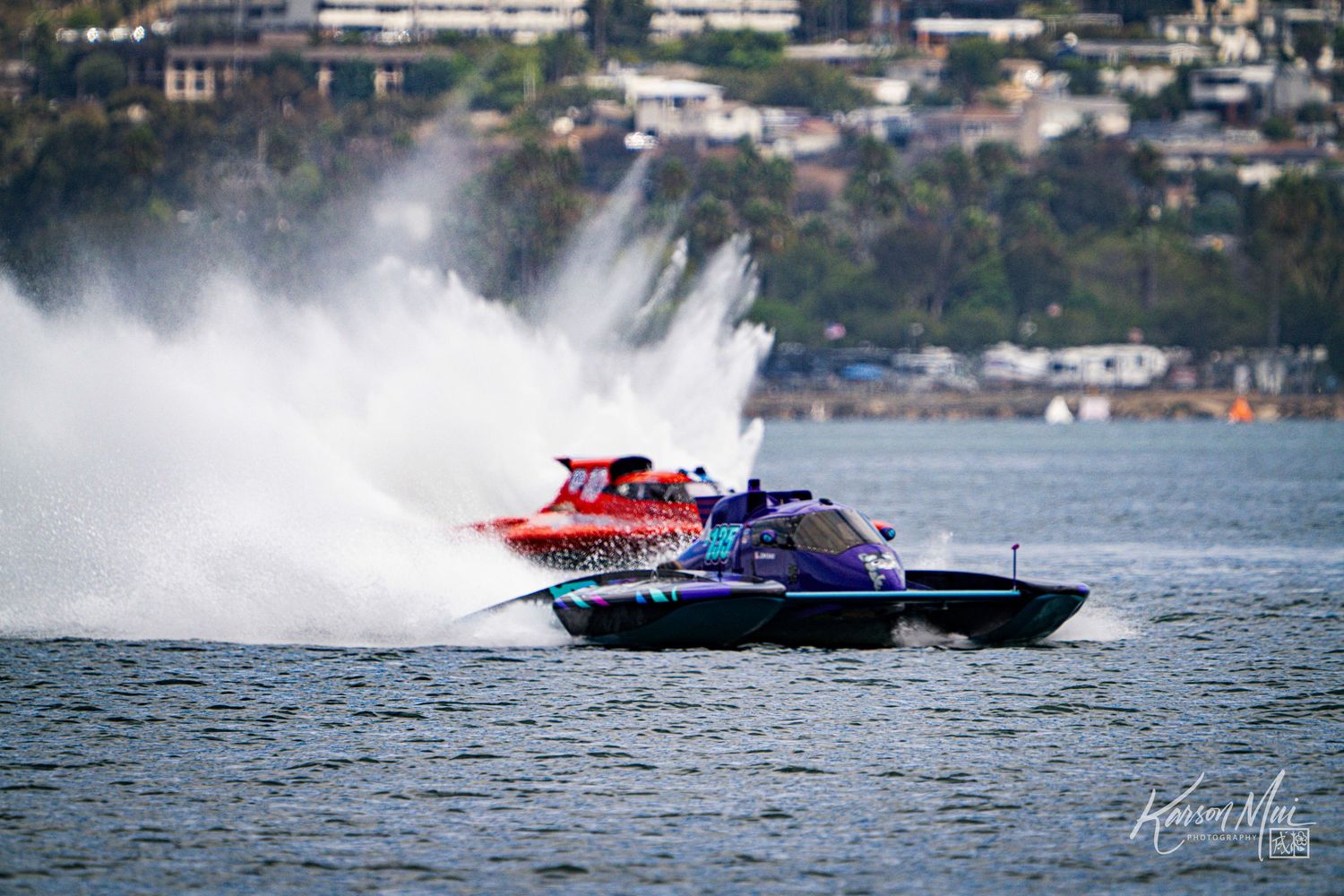 Red and purple powerboats race competitively across open water creating dramatic white water spray.