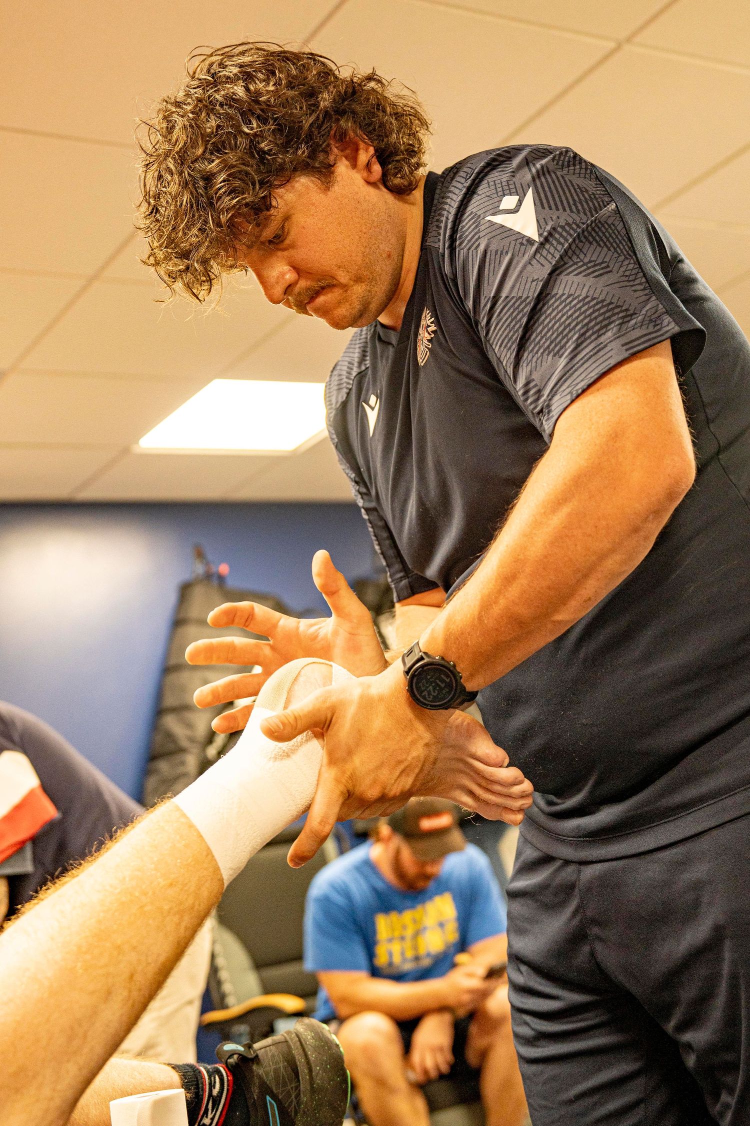 Curly-haired athletic trainer wraps a player's wrist in a sports training facility.