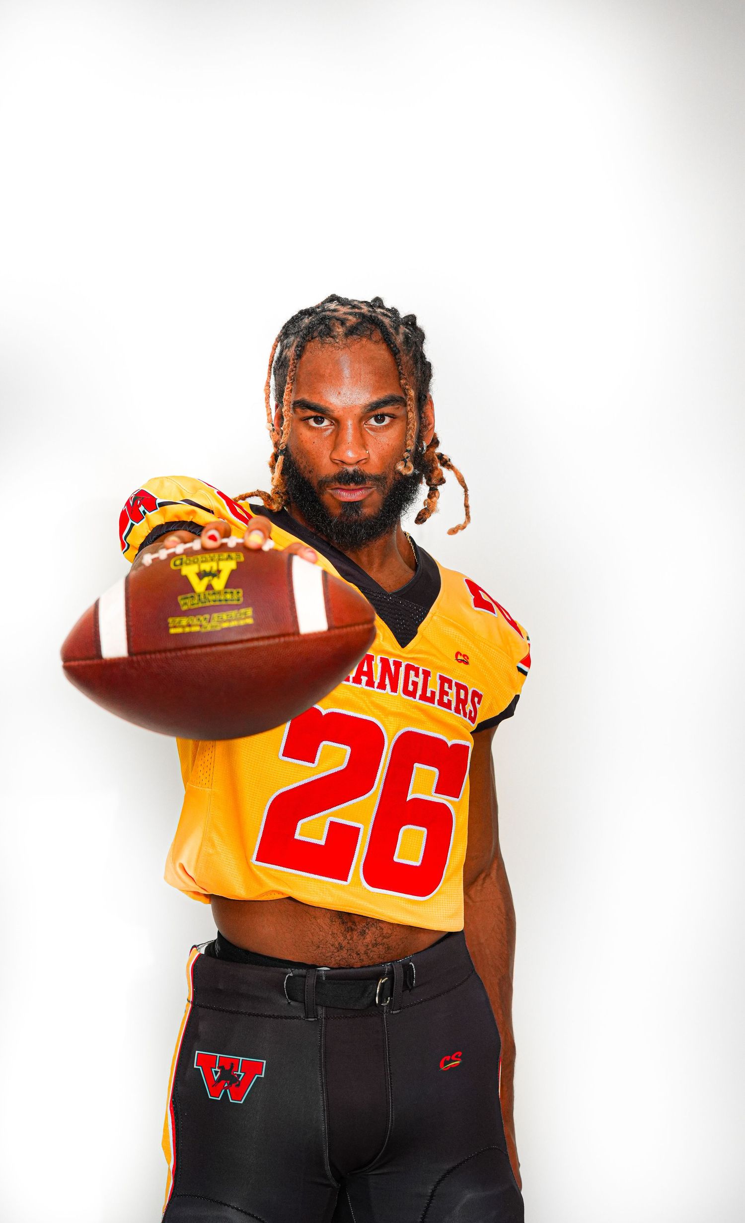Football player in gold Wranglers #26 jersey holds ball toward camera in studio portrait.