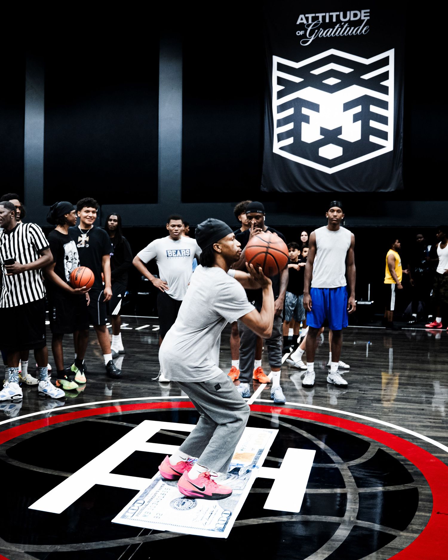 Player shoots a basketball at an indoor court event with crowd watching, Attitude of Gratitude banner displayed above.