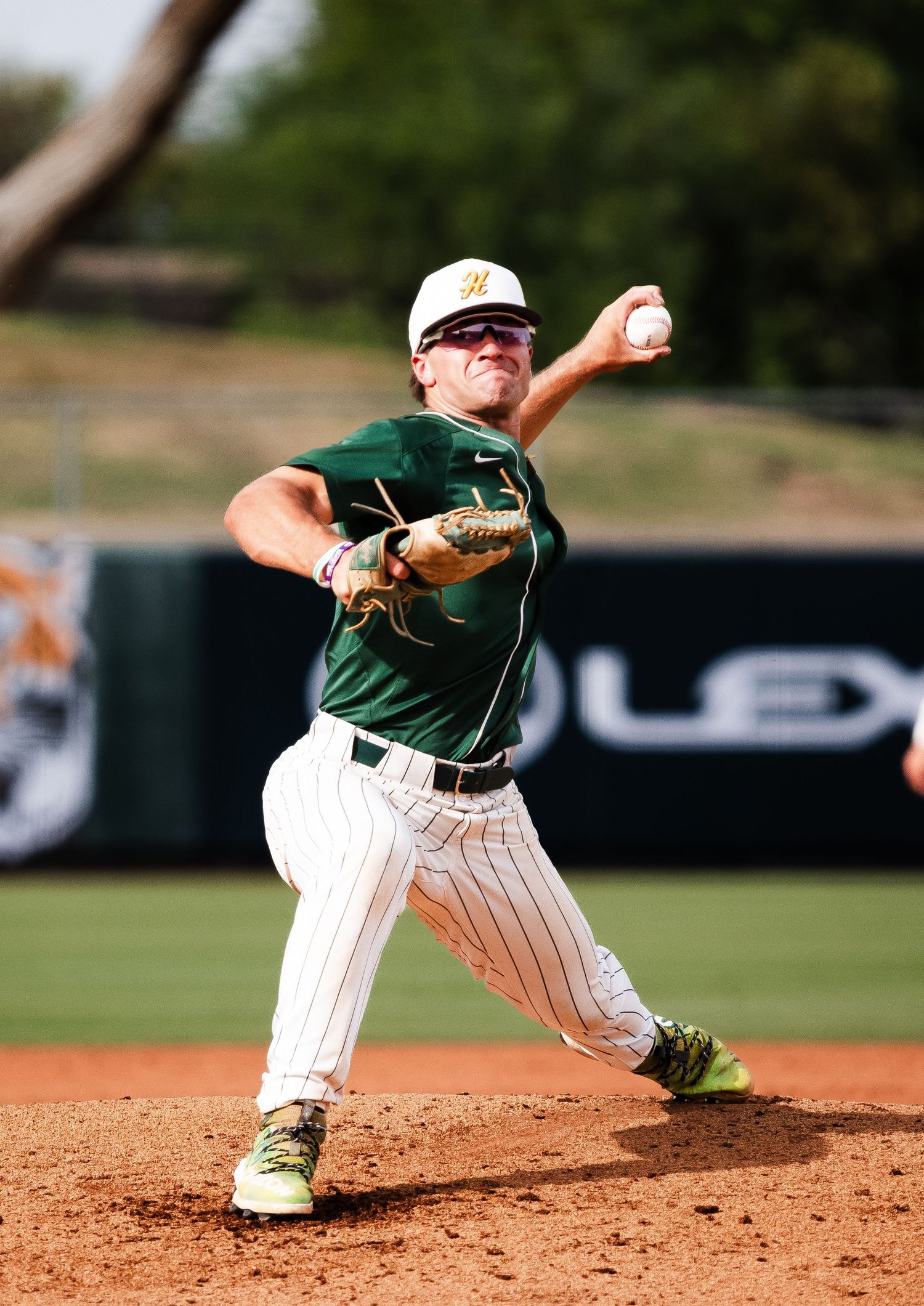 Baseball pitcher in green uniform mid-throw on mound during sunny outdoor game.