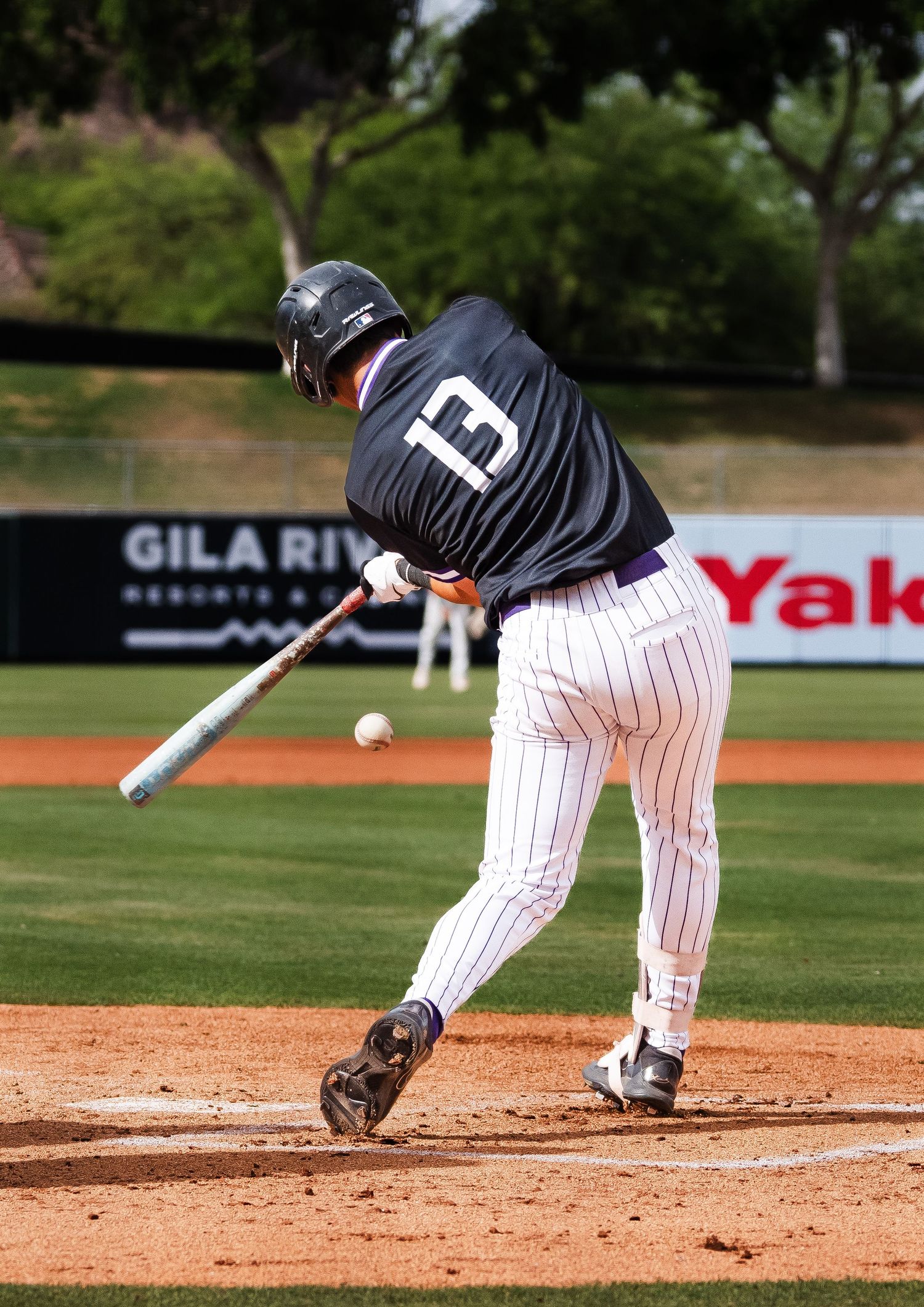 Baseball batter #13 swings at a pitch during a college baseball game at Gila River stadium.