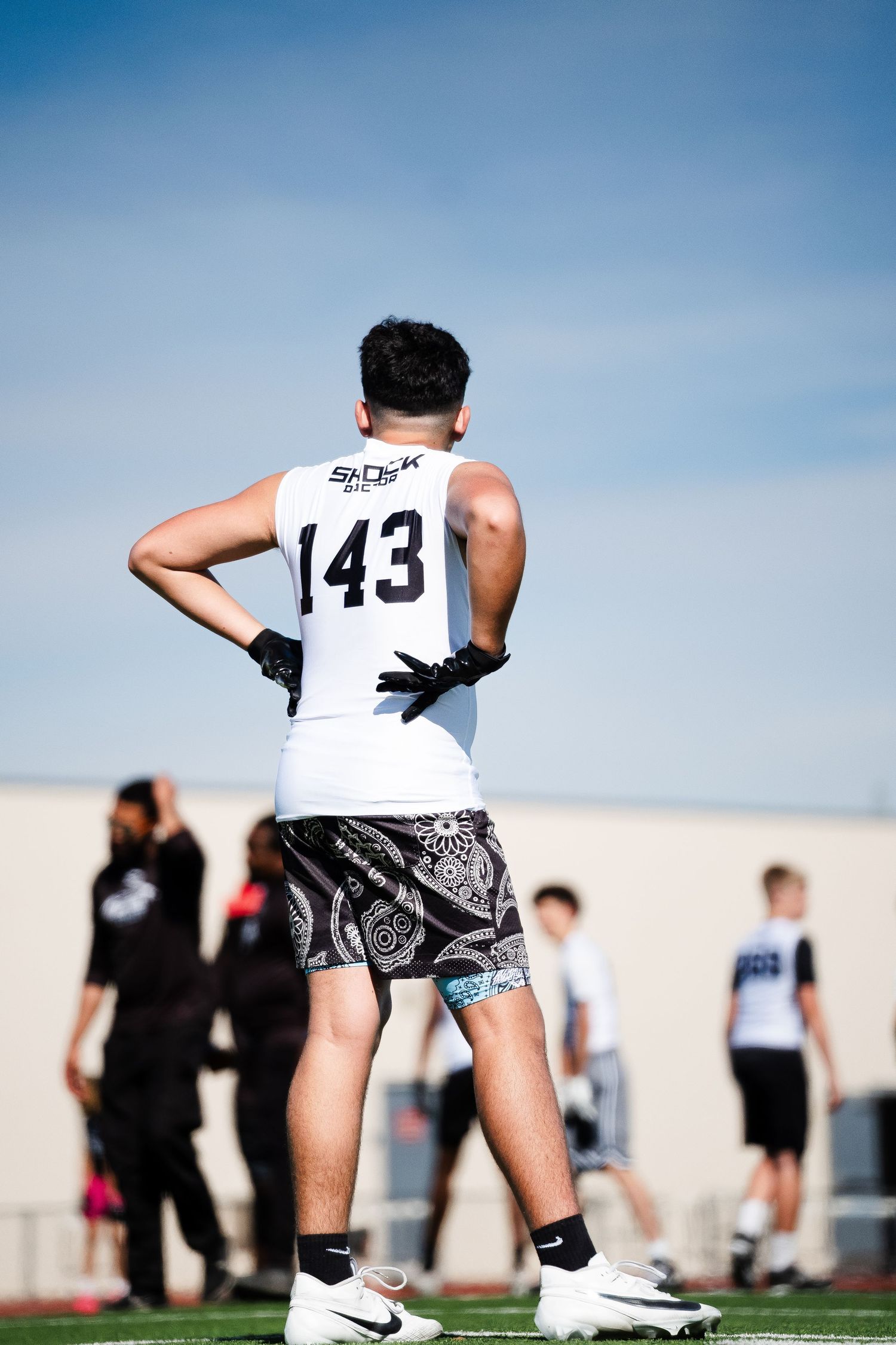 Athlete #143 in Shock jersey and patterned shorts stands on turf field at football combine.