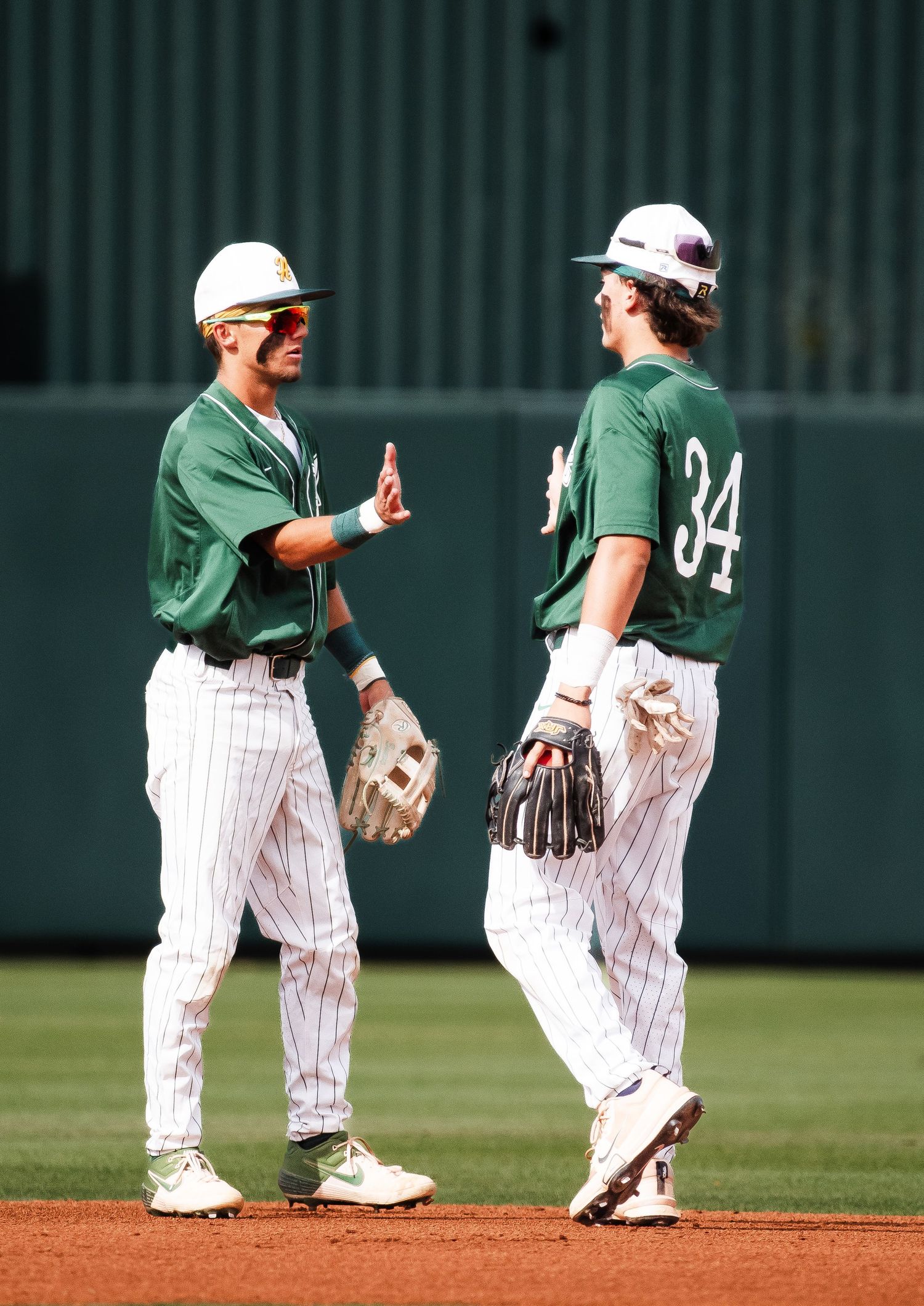 Two baseball teammates in green pinstripe uniforms celebrating on field.