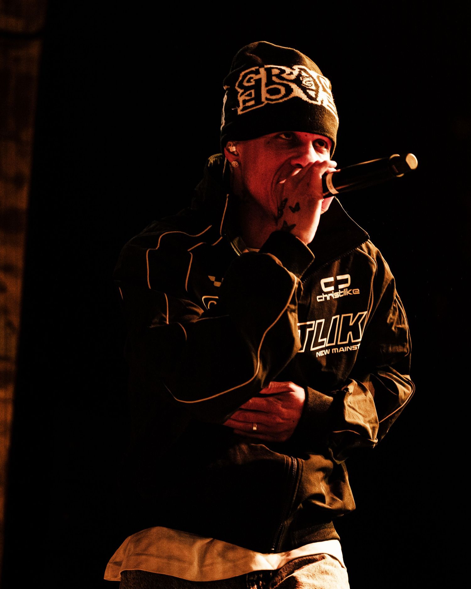 A rapper performs on stage wearing a beanie and black jacket while holding a microphone close to his mouth.
