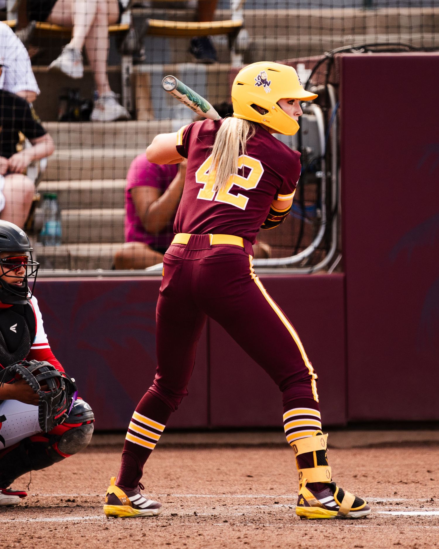 Softball player #42 in maroon and gold uniform batting stance wearing yellow helmet at college softball game.