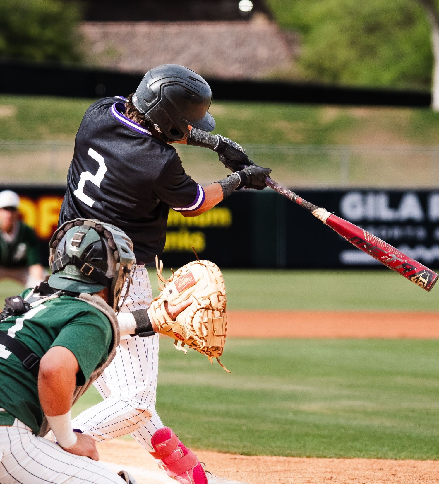 Baseball batter wearing number 2 jersey swings at pitch while catcher crouches behind home plate during game.