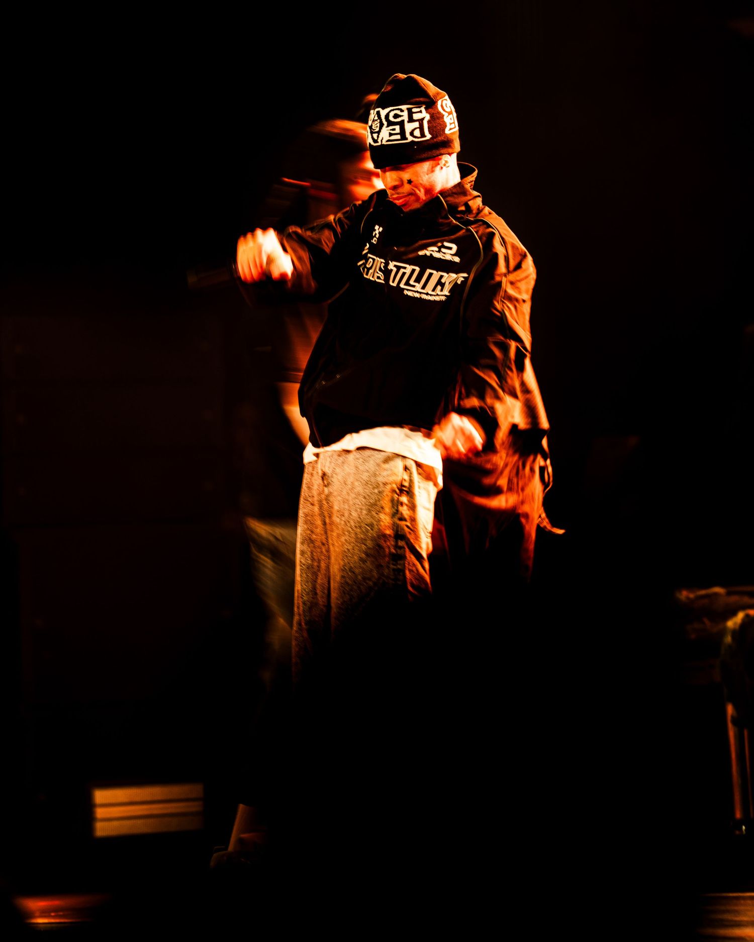A dynamic hip-hop performer dances energetically on stage under warm amber lighting.