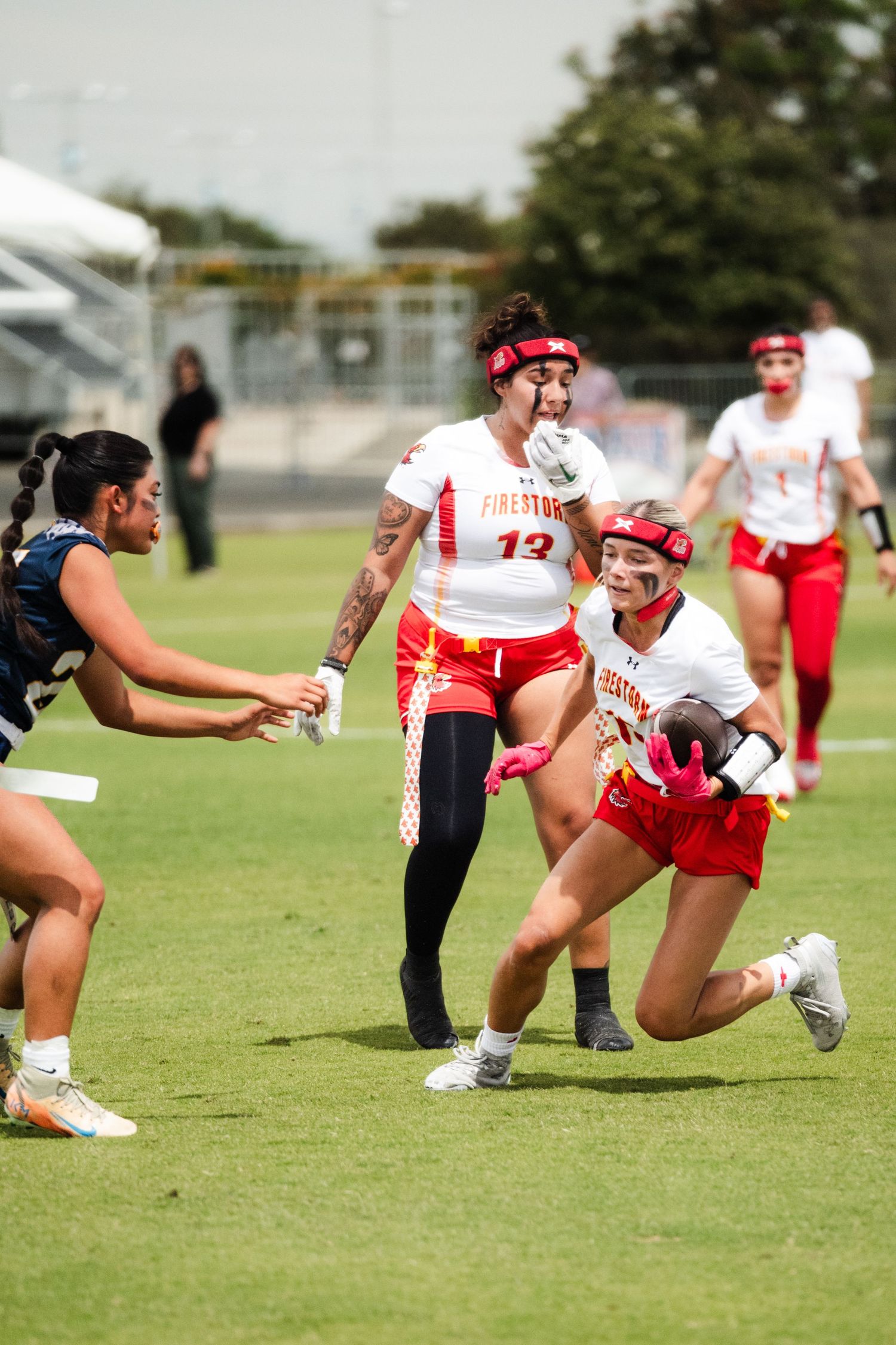 Women's flag football players in red uniforms competing on field, one player lunging to grab flag.