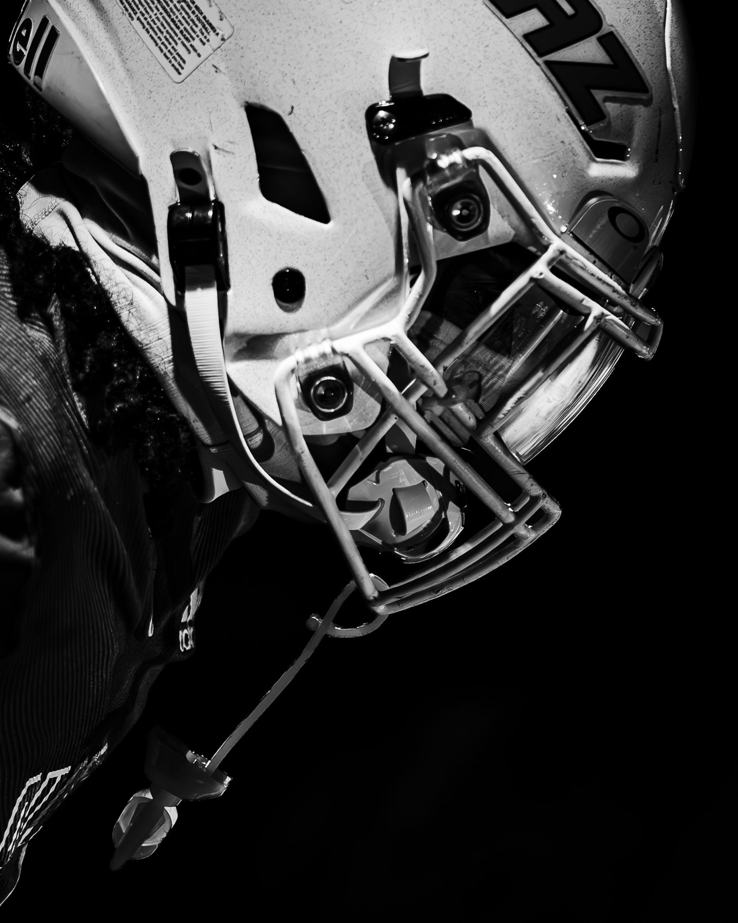 Close-up black and white photo of an American football helmet with face mask against a dark background.