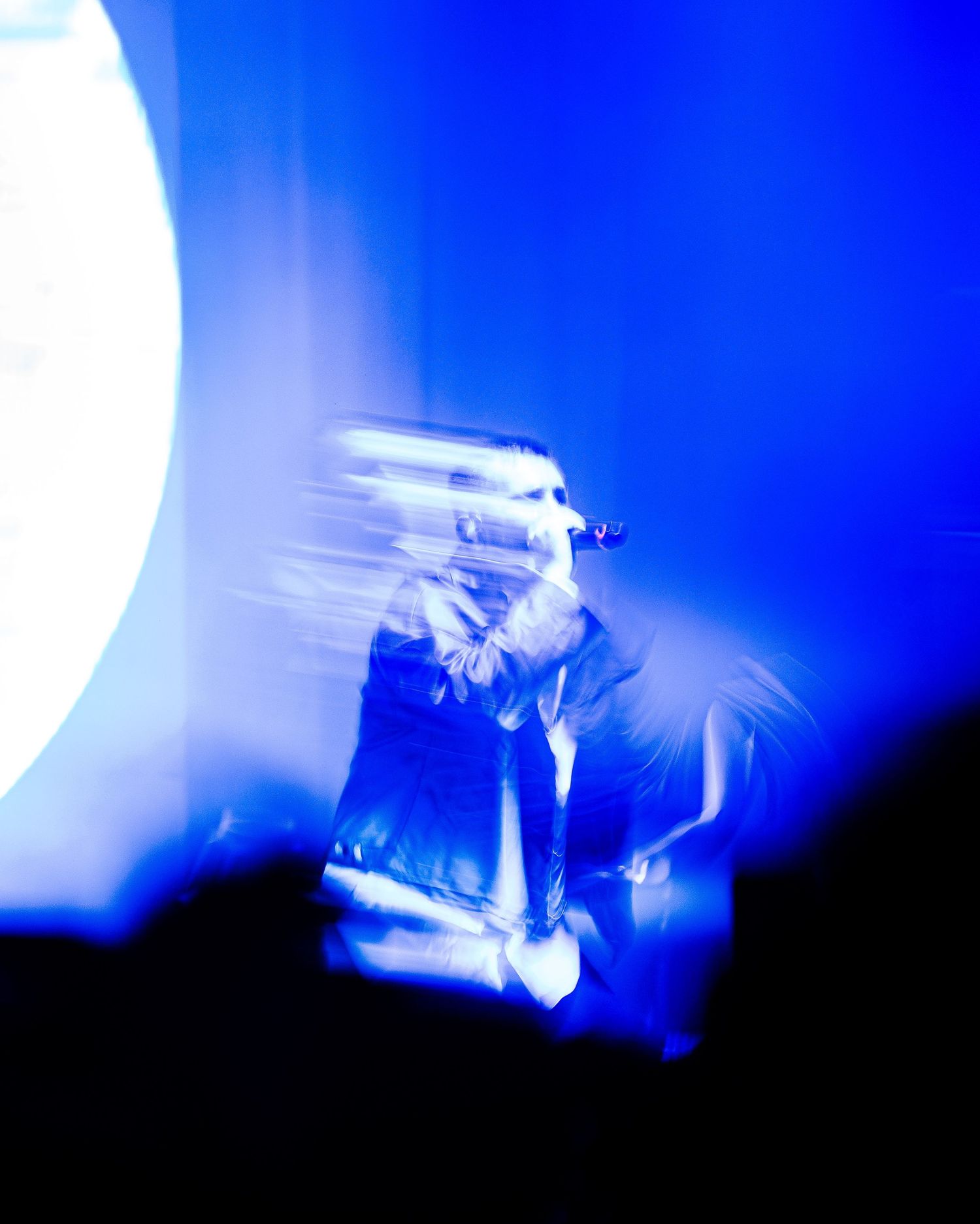 A singer performs on stage bathed in blue light with motion blur effects during a live concert.