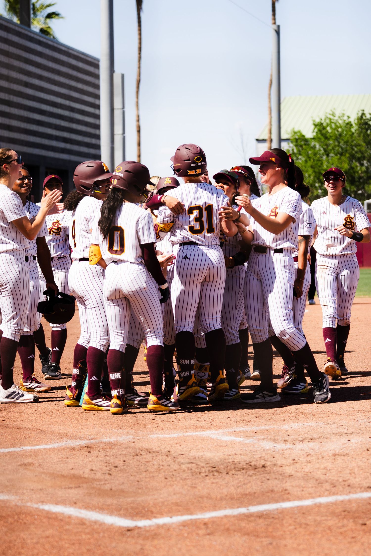 College softball team in maroon pinstripe uniforms celebrates together at home plate after a home run score.