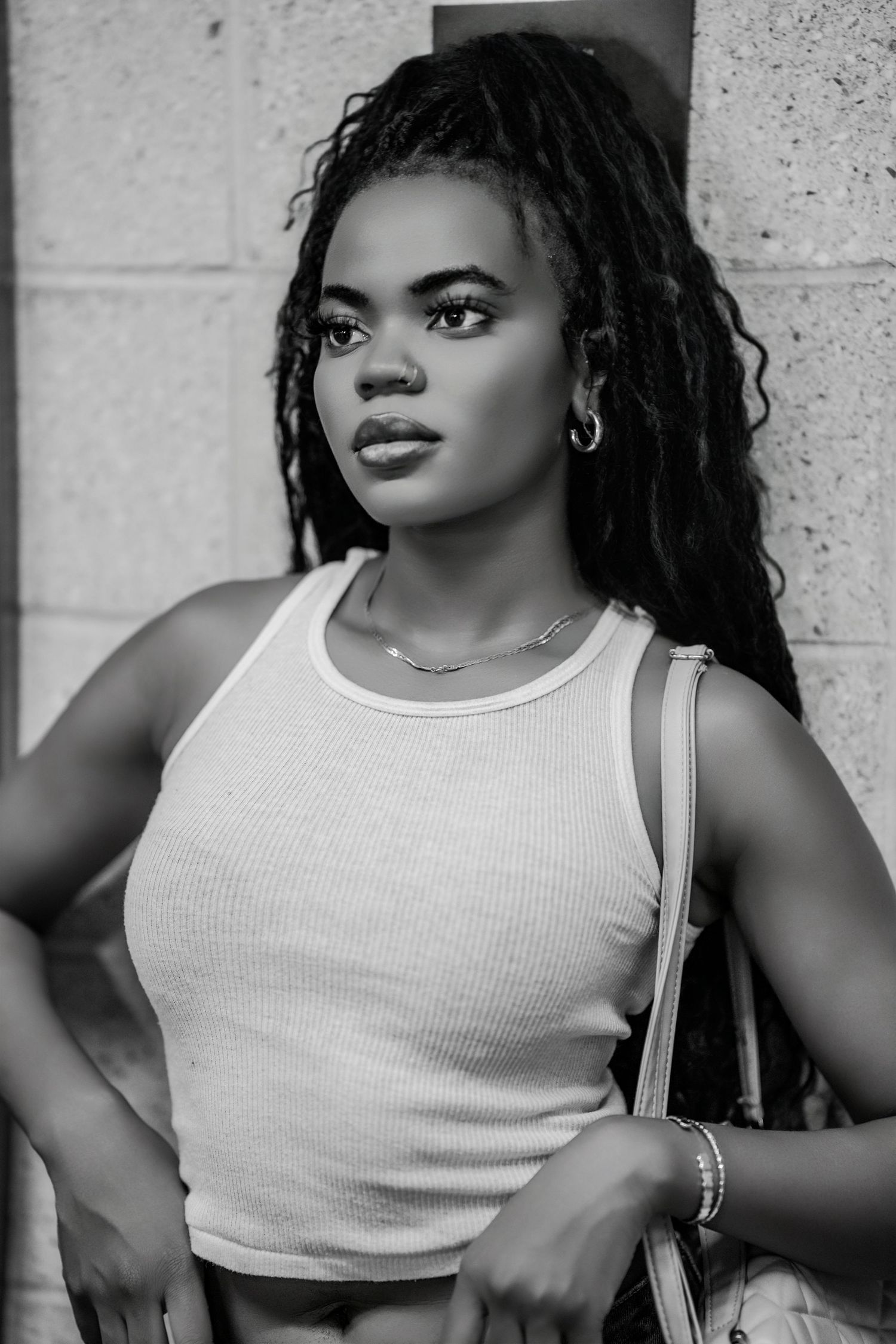Black and white close-up portrait of a young woman with braids wearing a white ribbed tank top and chain necklace.