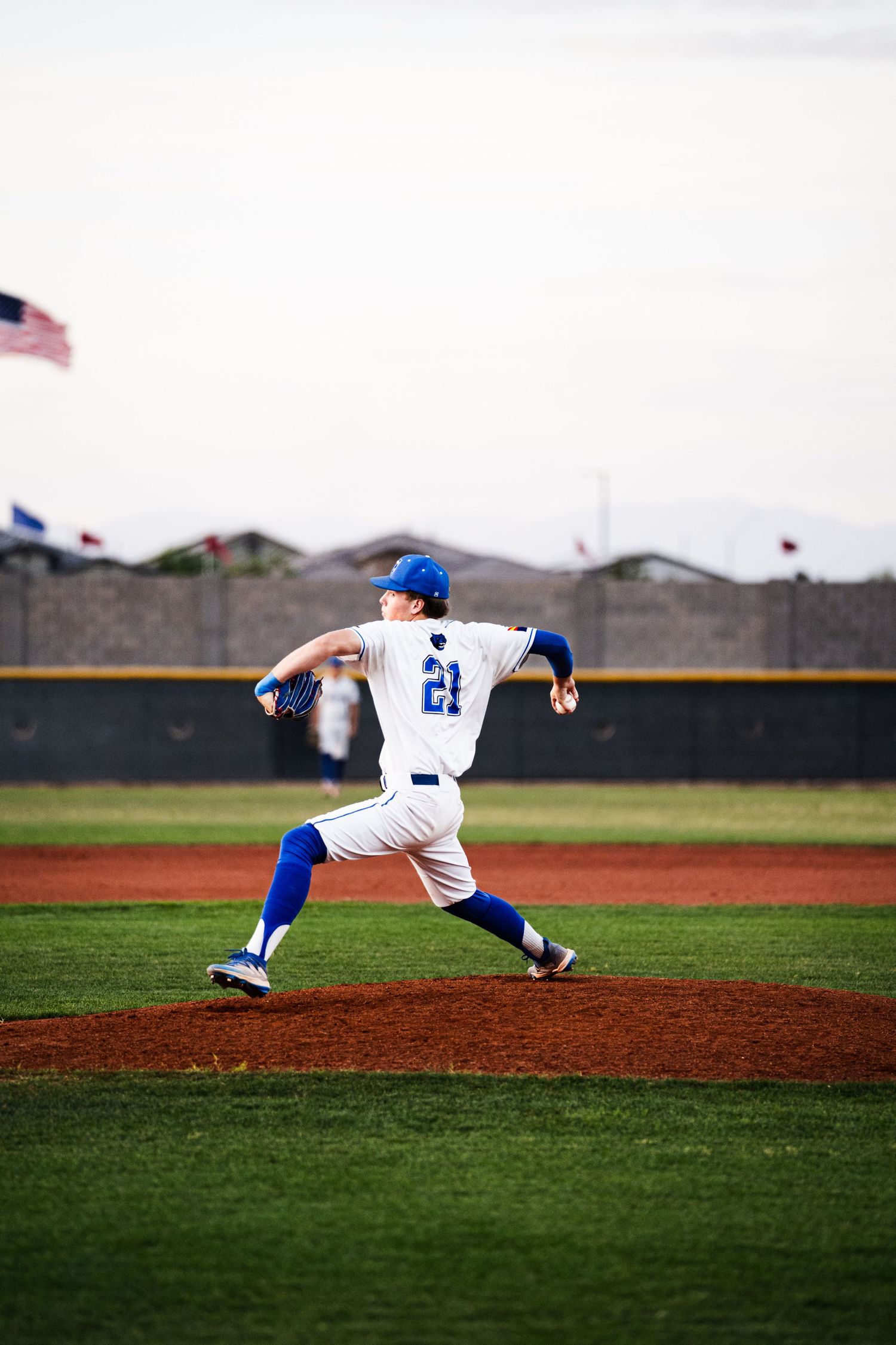 Baseball pitcher #21 in white and blue uniform mid-windup on pitching mound during a game.