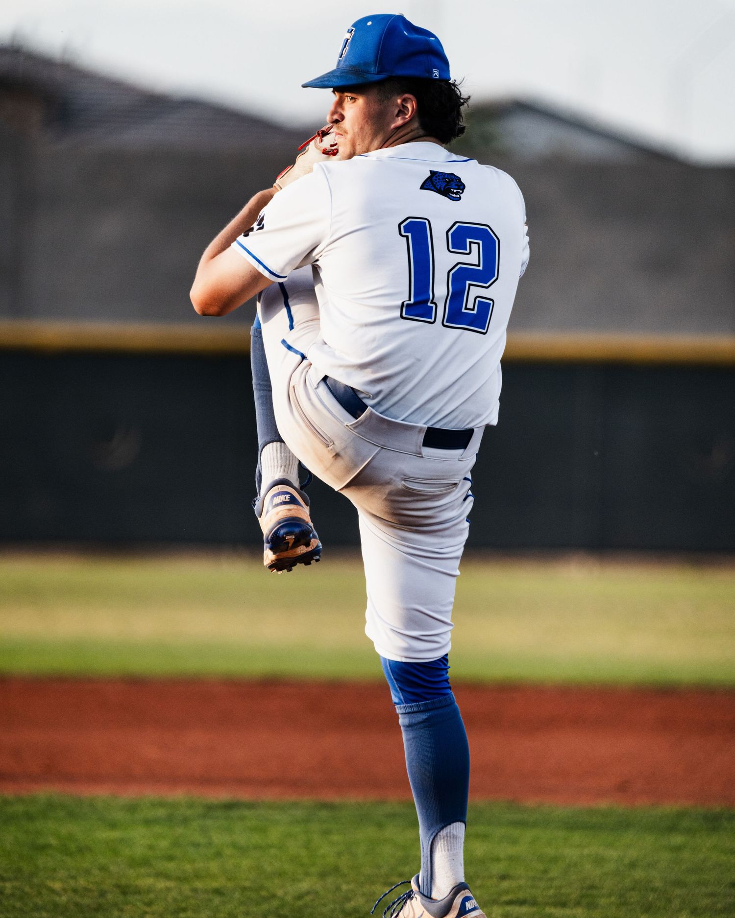 Baseball pitcher #12 in white and blue uniform mid-windup on the mound during a game.