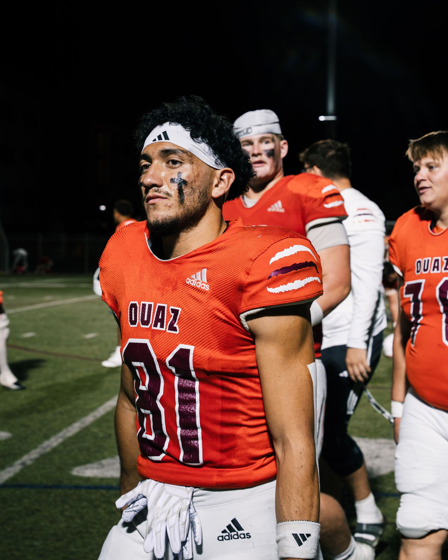 OUAZ football player #81 in orange Adidas jersey on field at night game with teammates in background.