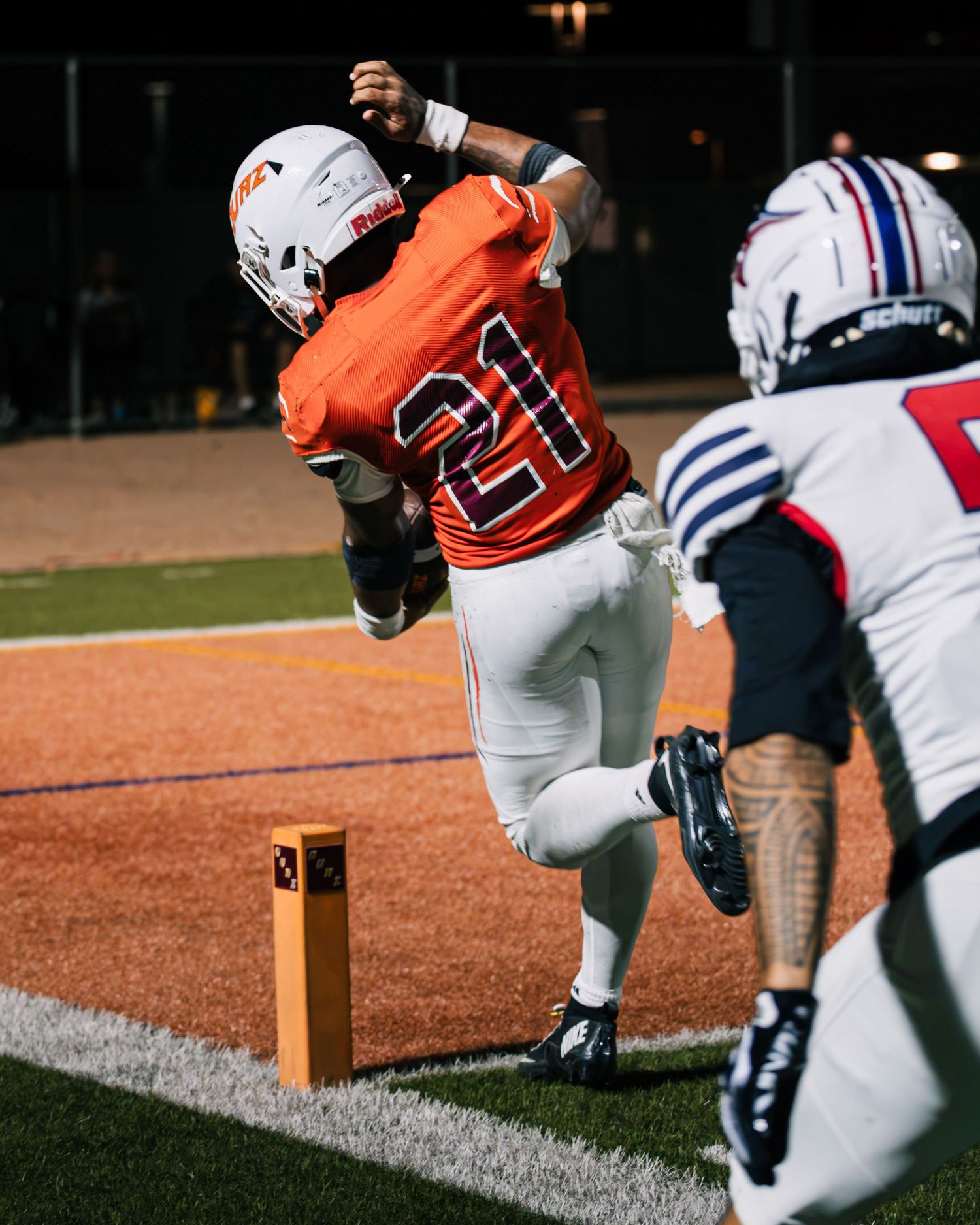 Football player #21 in orange jersey scores a touchdown near the pylon during a night game.