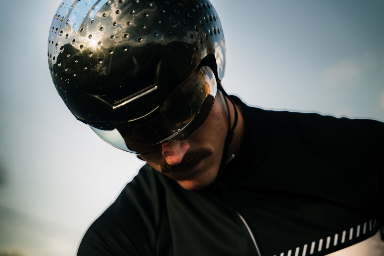 Close-up of cyclist wearing sleek black aerodynamic helmet and sunglasses in low light conditions.