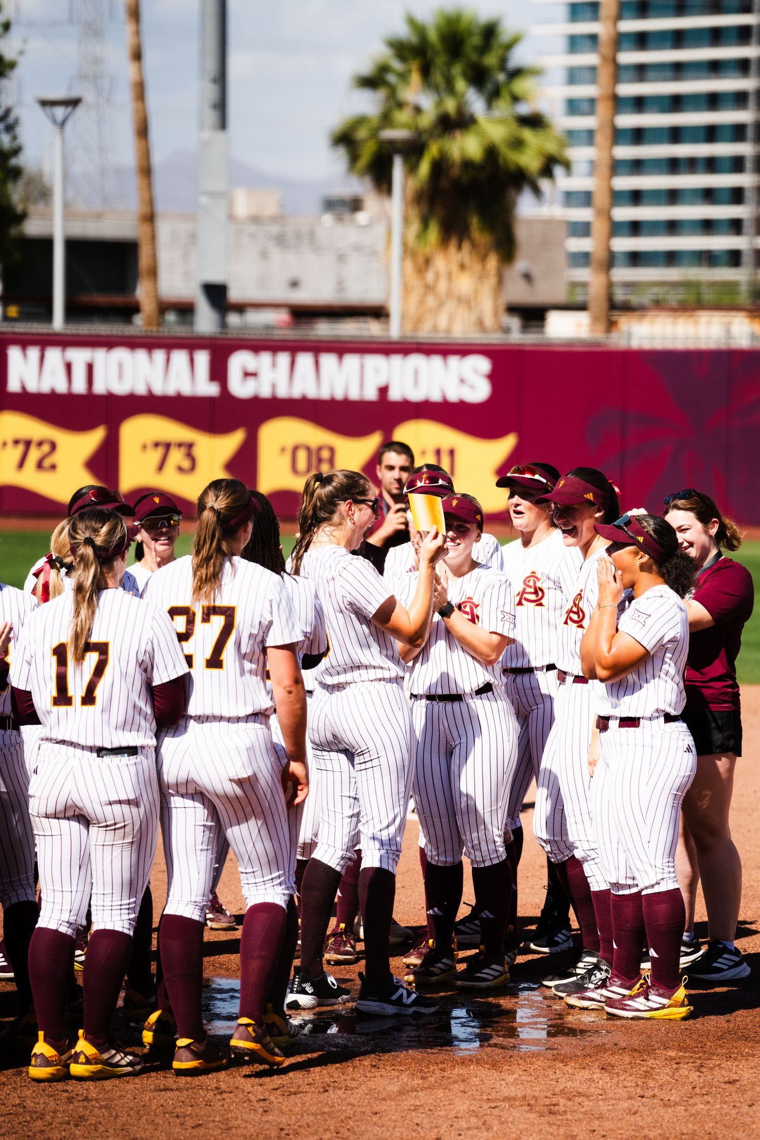 ASU Sun Devils softball team celebrating together on the field in front of National Champions banner.