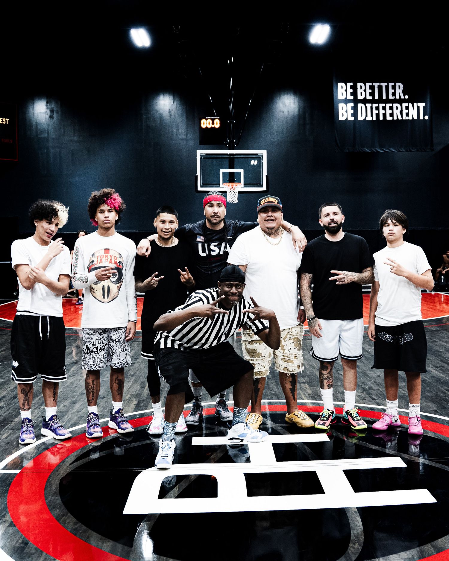 Group of eight people posing on a basketball court with 'Be Better. Be Different.' slogan on the wall.